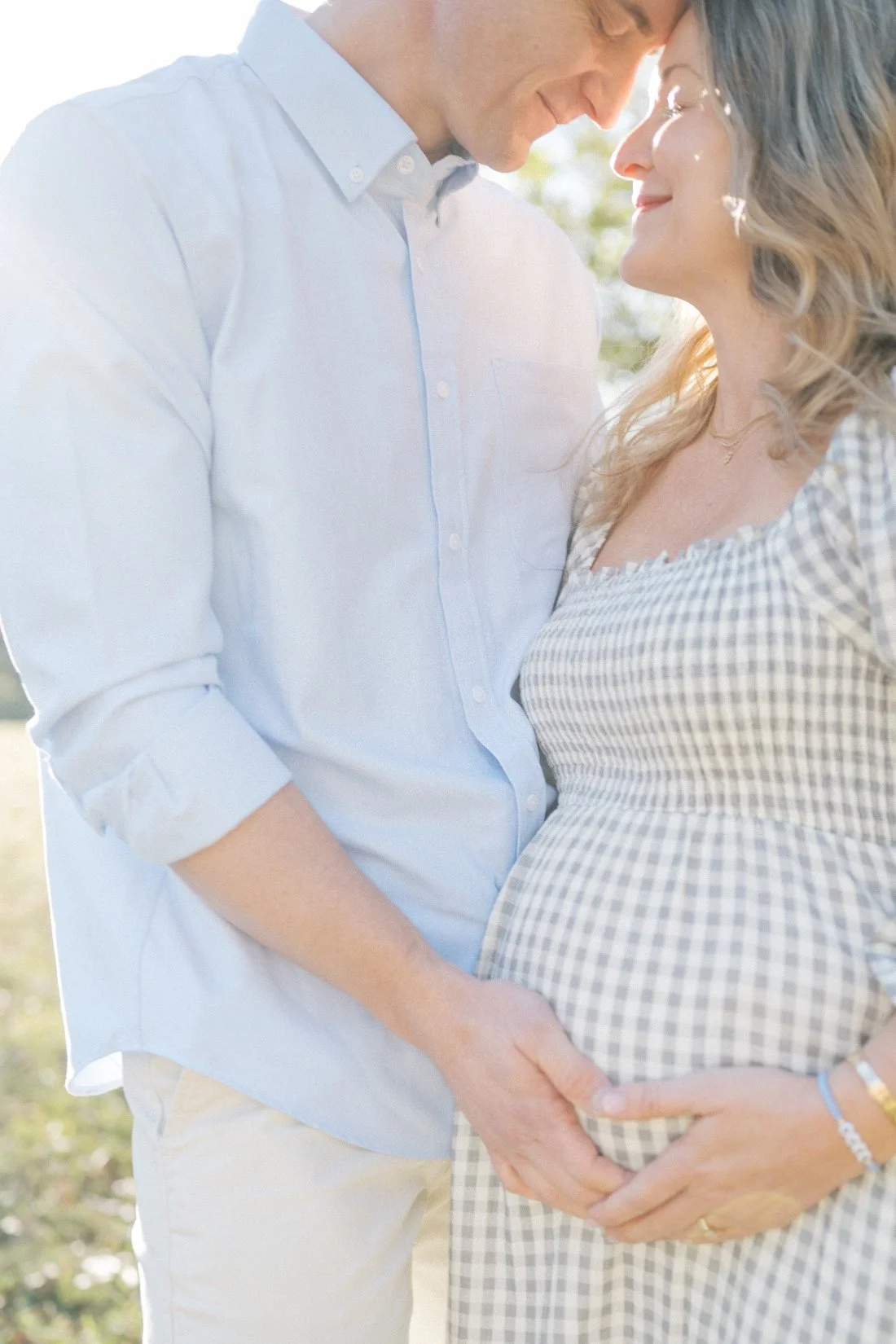 Couple standing close together outdoors, gently holding baby bump during soft light spring maternity photos