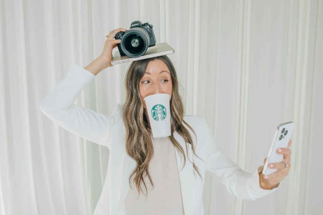 Kelly Bullock balancing her camera and laptop while holding coffee and a phone, showing the busy reality of managing a photography client experience.