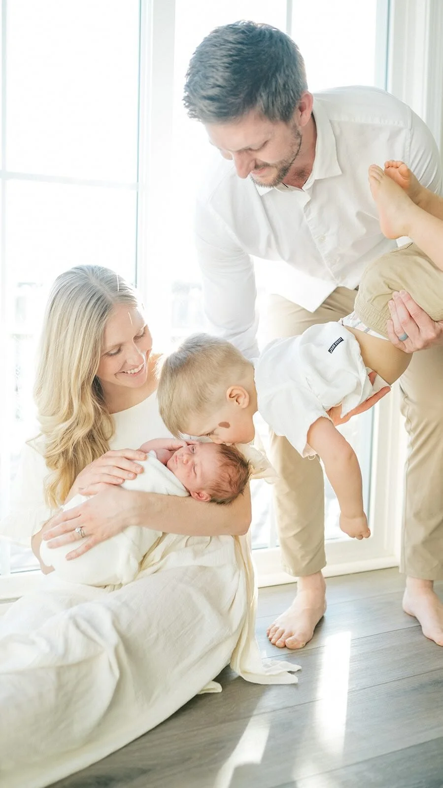 Mom holding baby while Dad helps big brother give baby a kiss - Raleigh Newborn Photographer