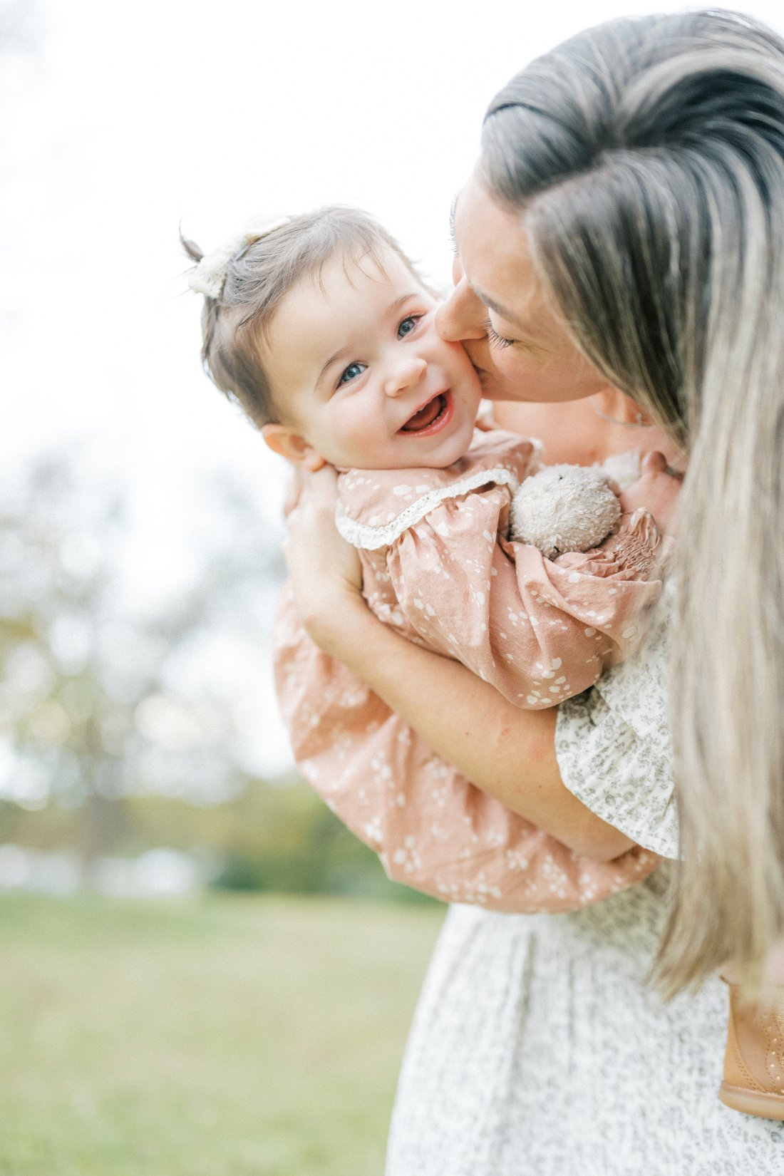 Mother kissing her smiling baby outdoors, reflecting photography business ideas focused on genuine connection and memorable family experiences.