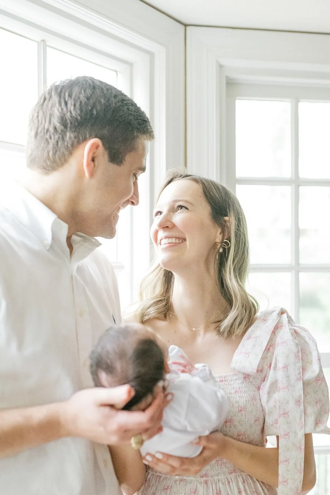 Mother and father holding baby looking at each other in natural light - Raleigh Newborn Photographer