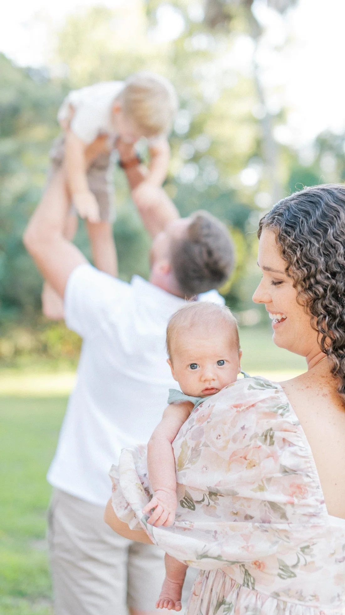 Mom holding her newborn while dad lifts their older son in the background, capturing family photos through the years from babyhood to early childhood