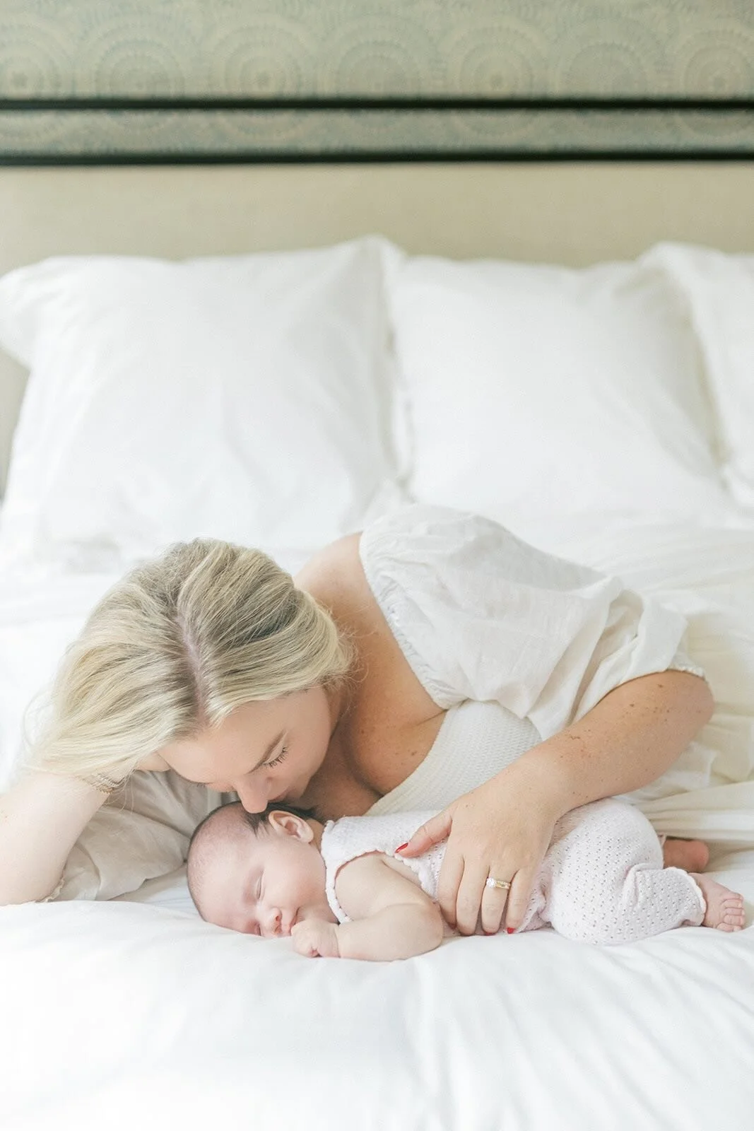 Mother giving sleeping baby a kiss while laying on the bed - Raleigh Newborn Photographer