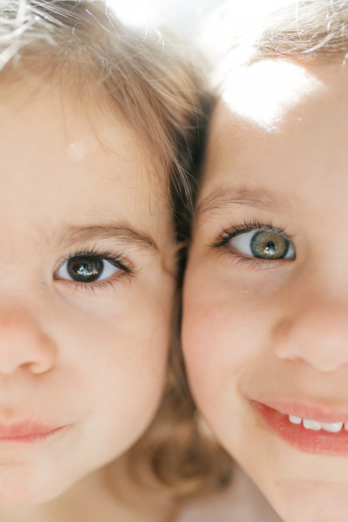Close up of two young children smiling with bright natural light highlighting their eyes, a sweet reminder of investing in memories through simple, everyday moments.