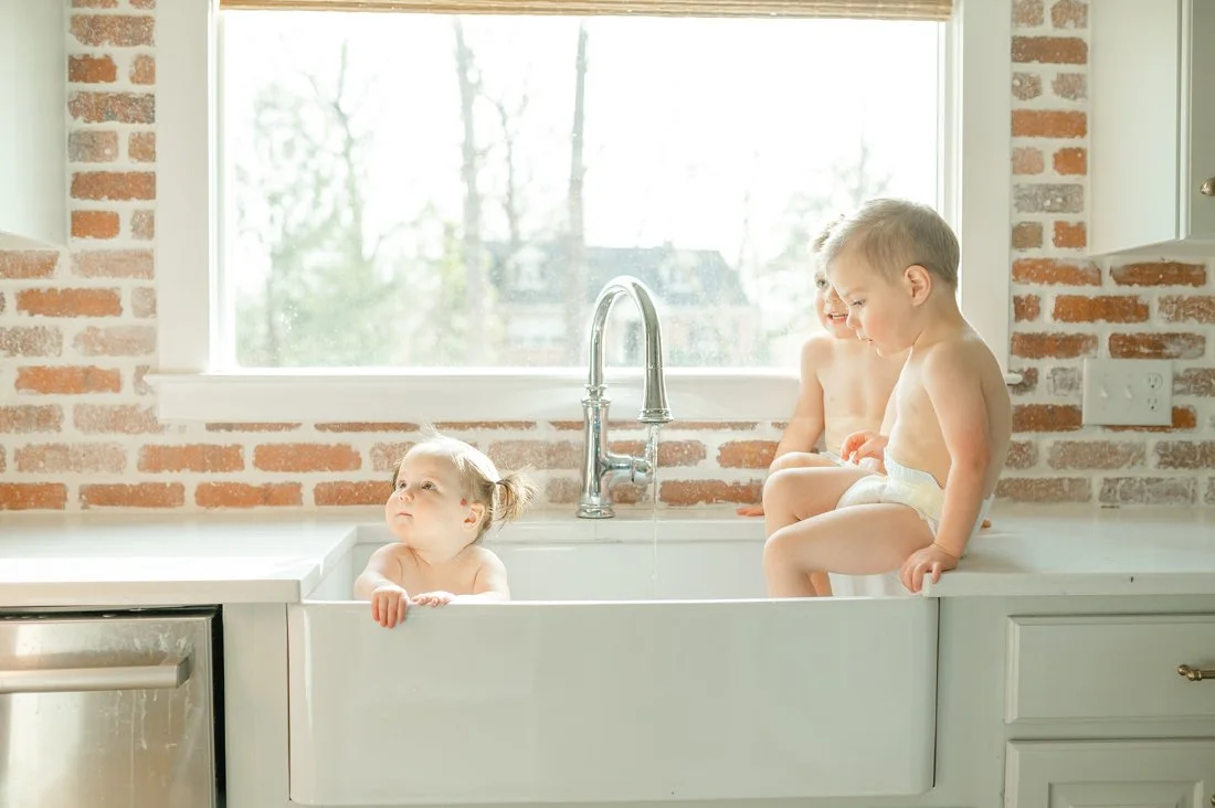 Three toddlers playing together in a sink, documenting playful everyday moments in family photos through the years