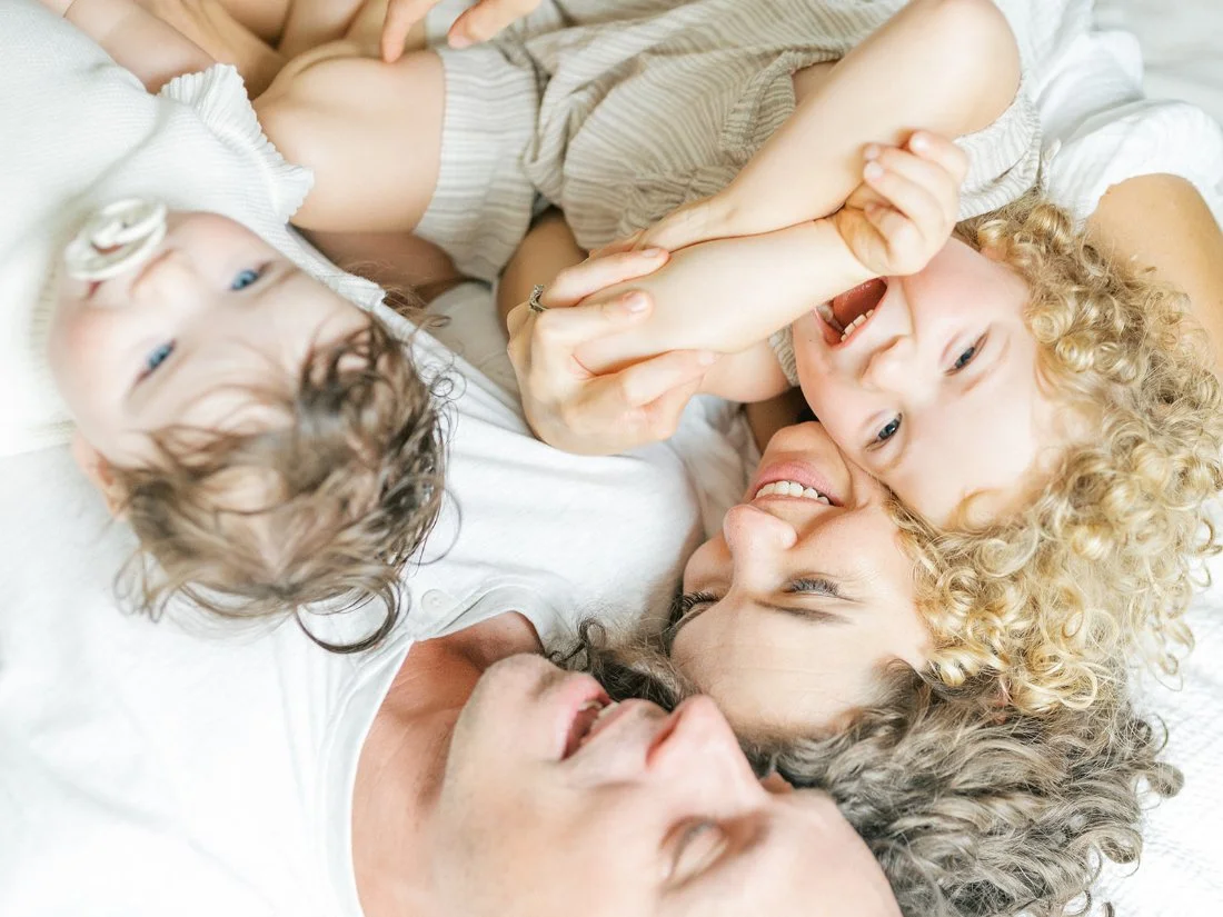 Playful family portraits showing parents laughing and cuddling with their children during a cozy indoor session.