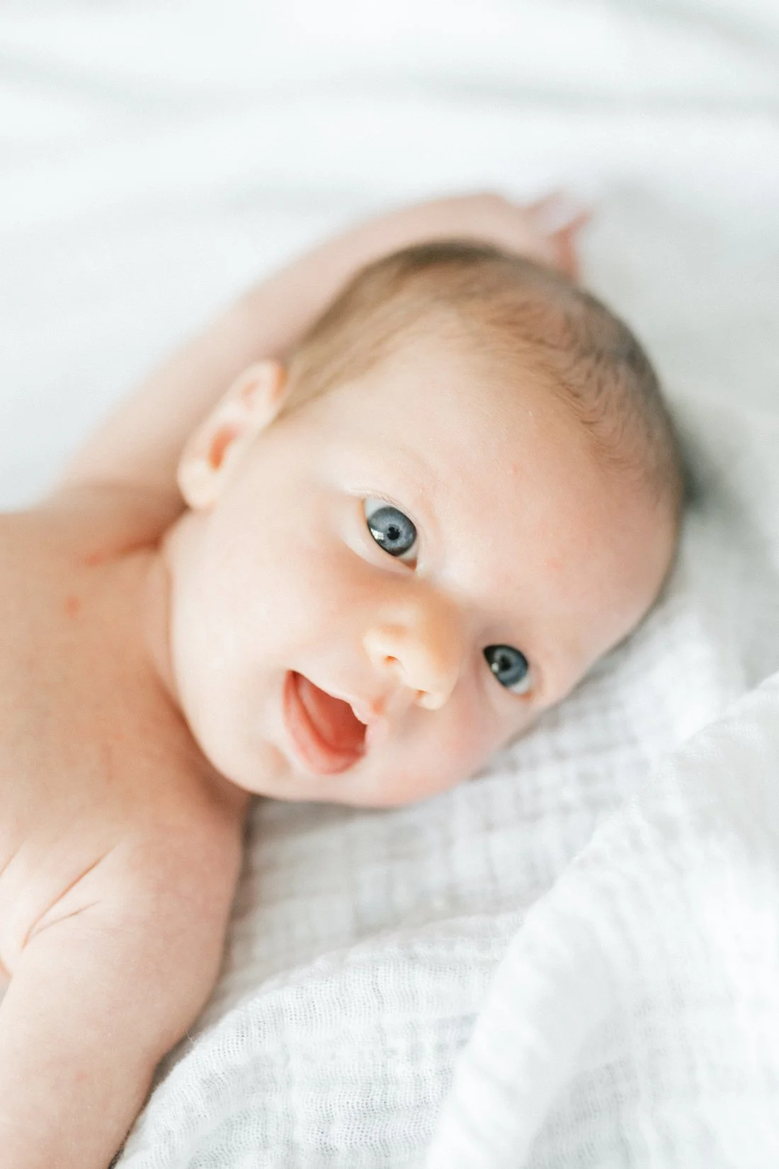 Soft newborn portrait often included in a grandparent photoshoot gallery, featuring a baby lying on a white blanket with bright, curious eyes.