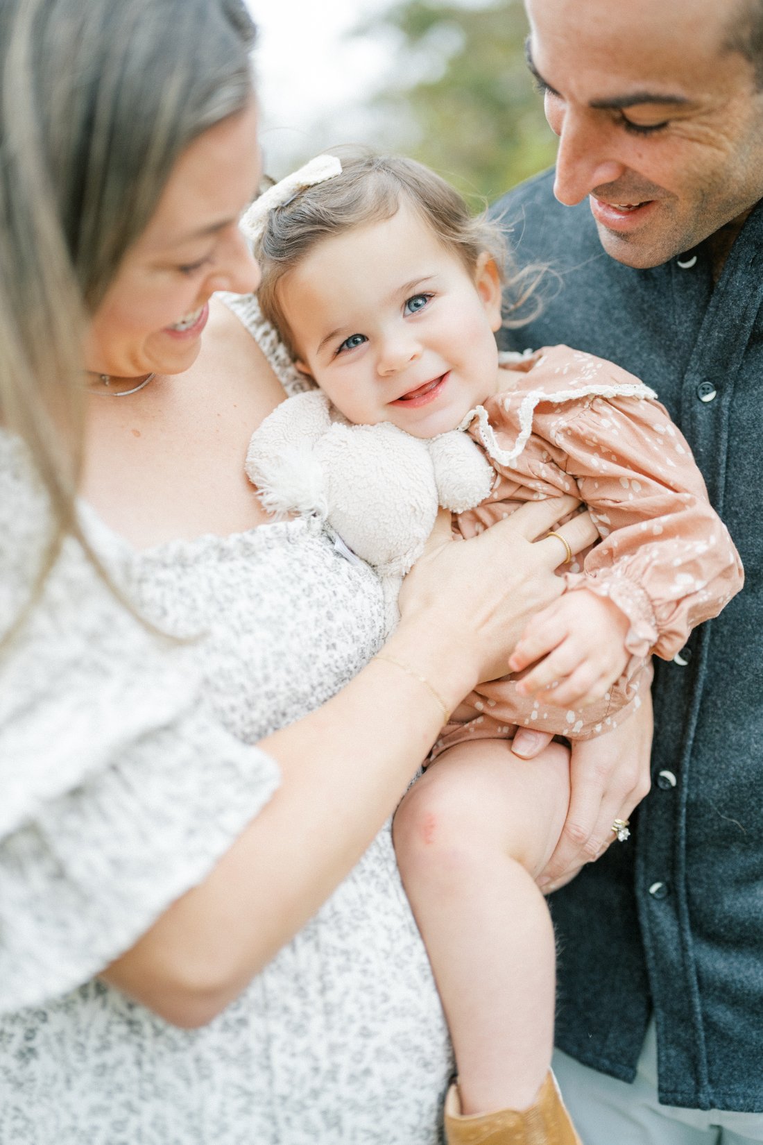 Natural family photos of parents cuddling their smiling toddler during a relaxed lifestyle family session in Raleigh.