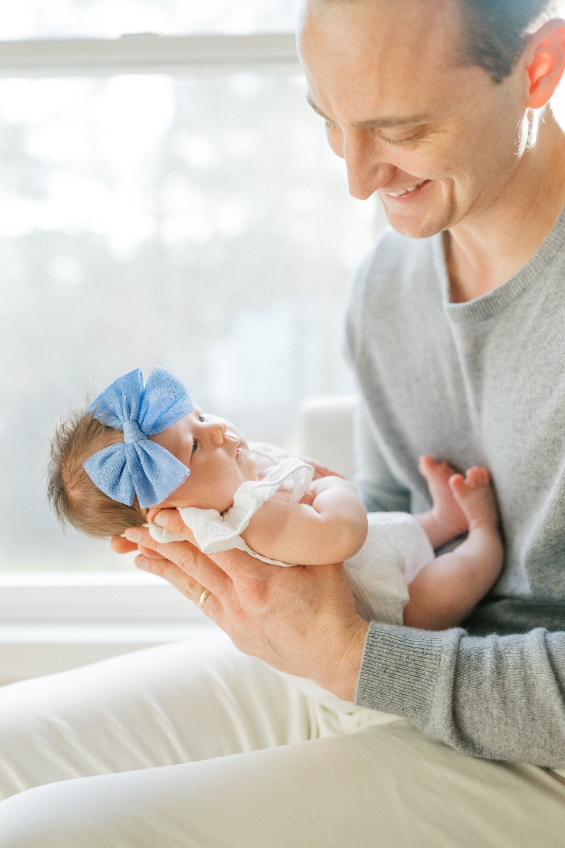 Father holding newborn baby by window light during intimate in-home milestone checklist session