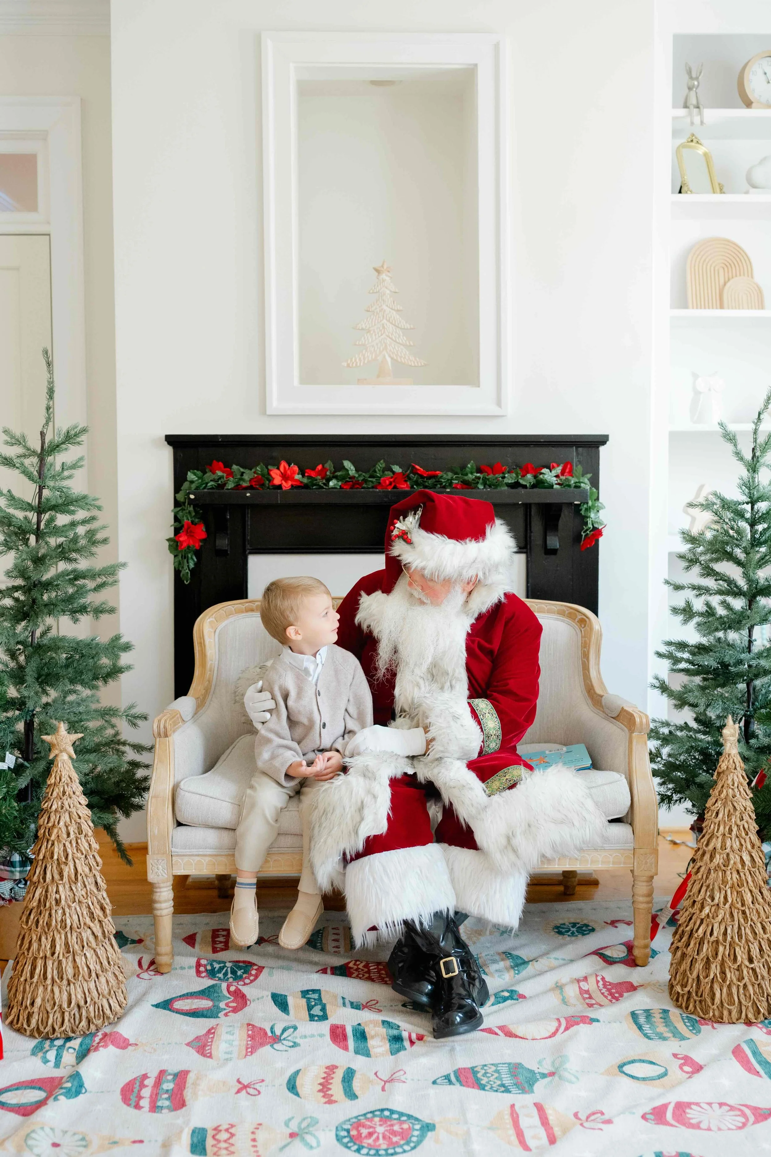 Little boy sitting next to Santa with awe in his eyes and wondering when she will stop believing in Santa by Kelly Bullock Photography.