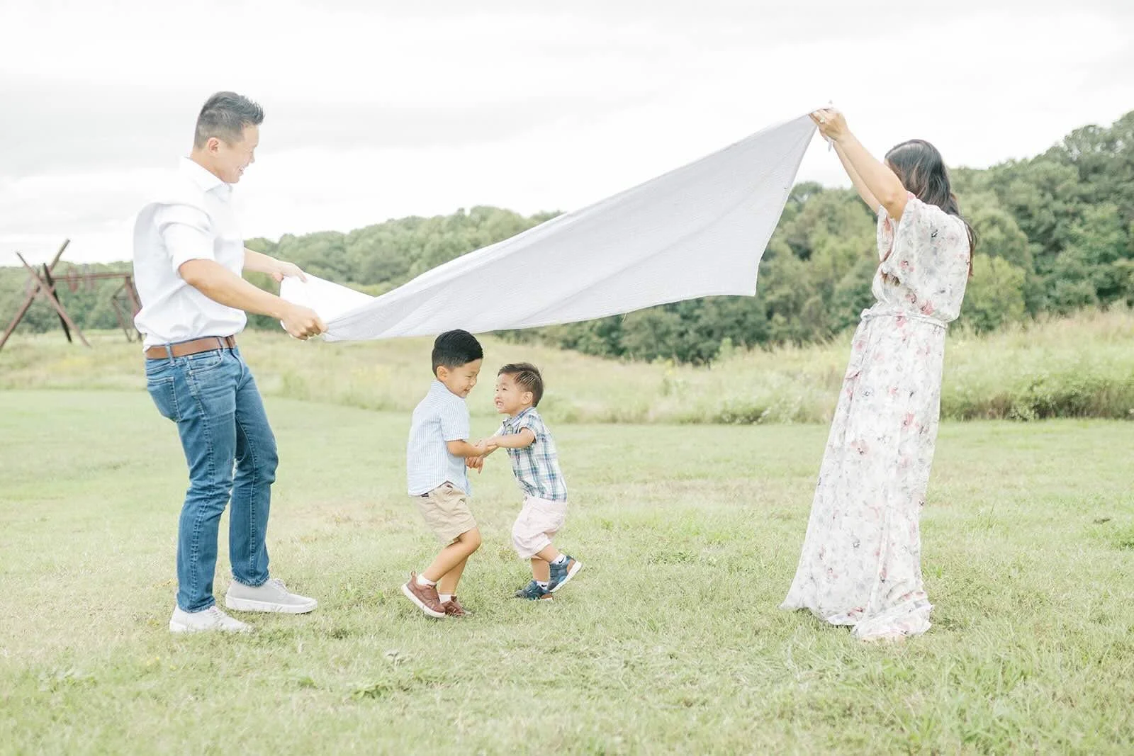 Mom and Dad holding up a blanket while sons play under it outside - Raleigh Newborn Photographer