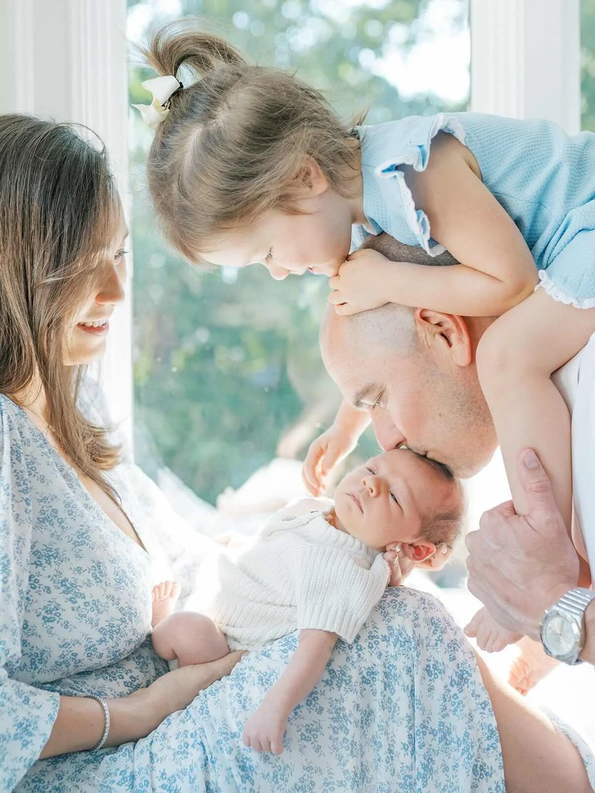 Mother holding baby while Father holds big sister on his shoulders and giving baby a kiss - Raleigh Newborn Photographer