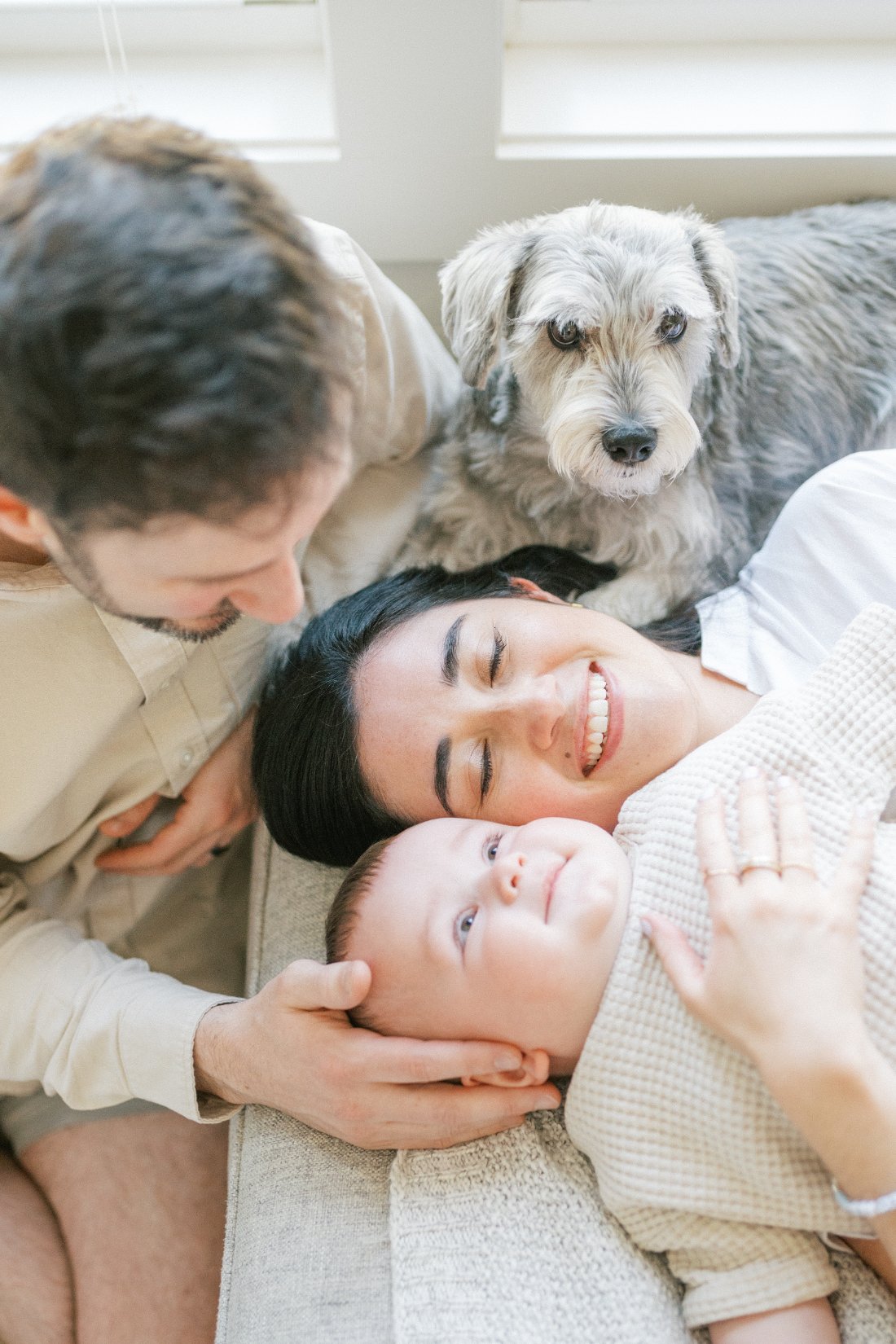 Family portraits with dogs at home featuring parents cuddling newborn while dog rests nearby on couch