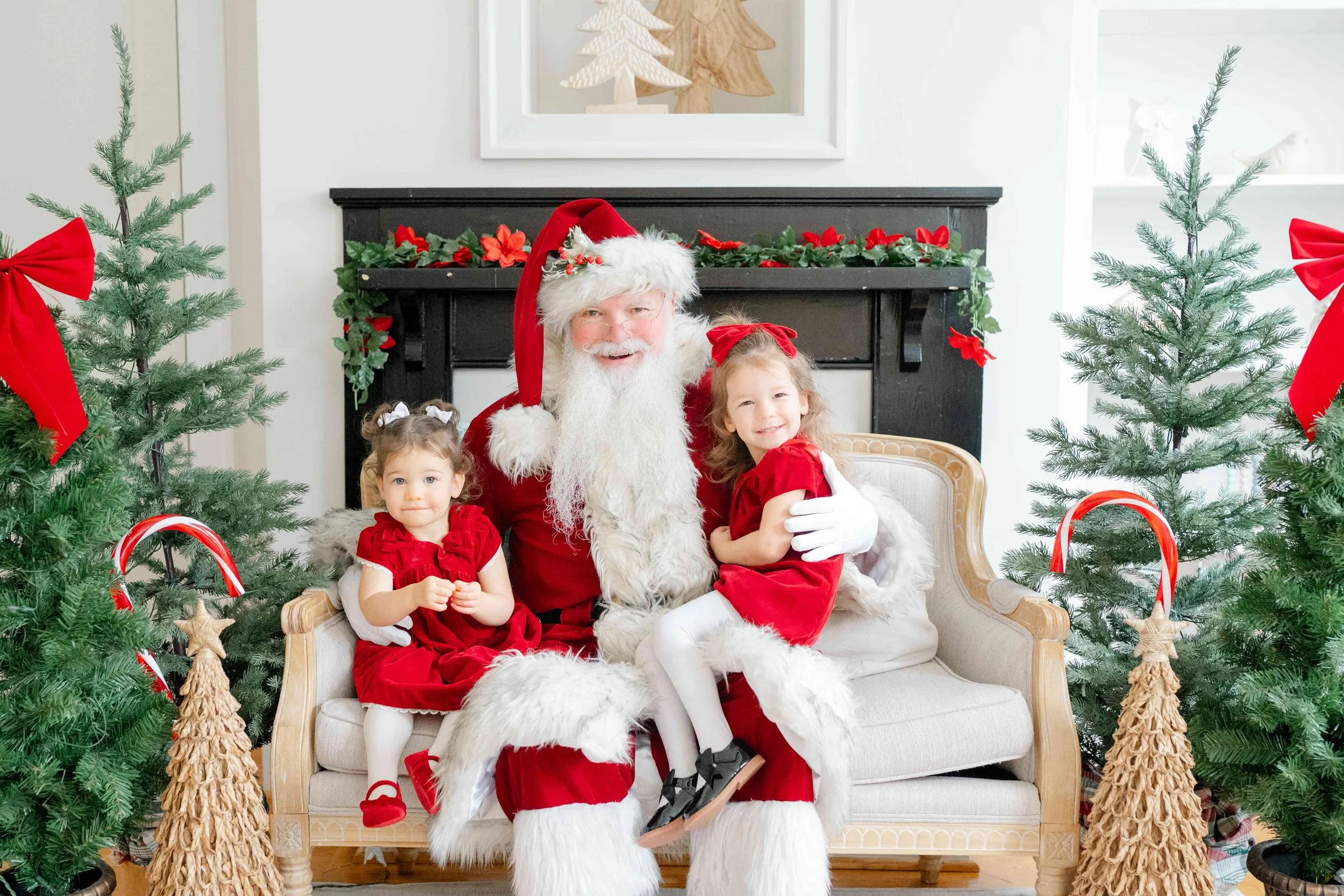 Two girls sitting next to Santa on the couch and smiling during their family Christmas Activity in Raleigh by Kelly Bullock Photography.