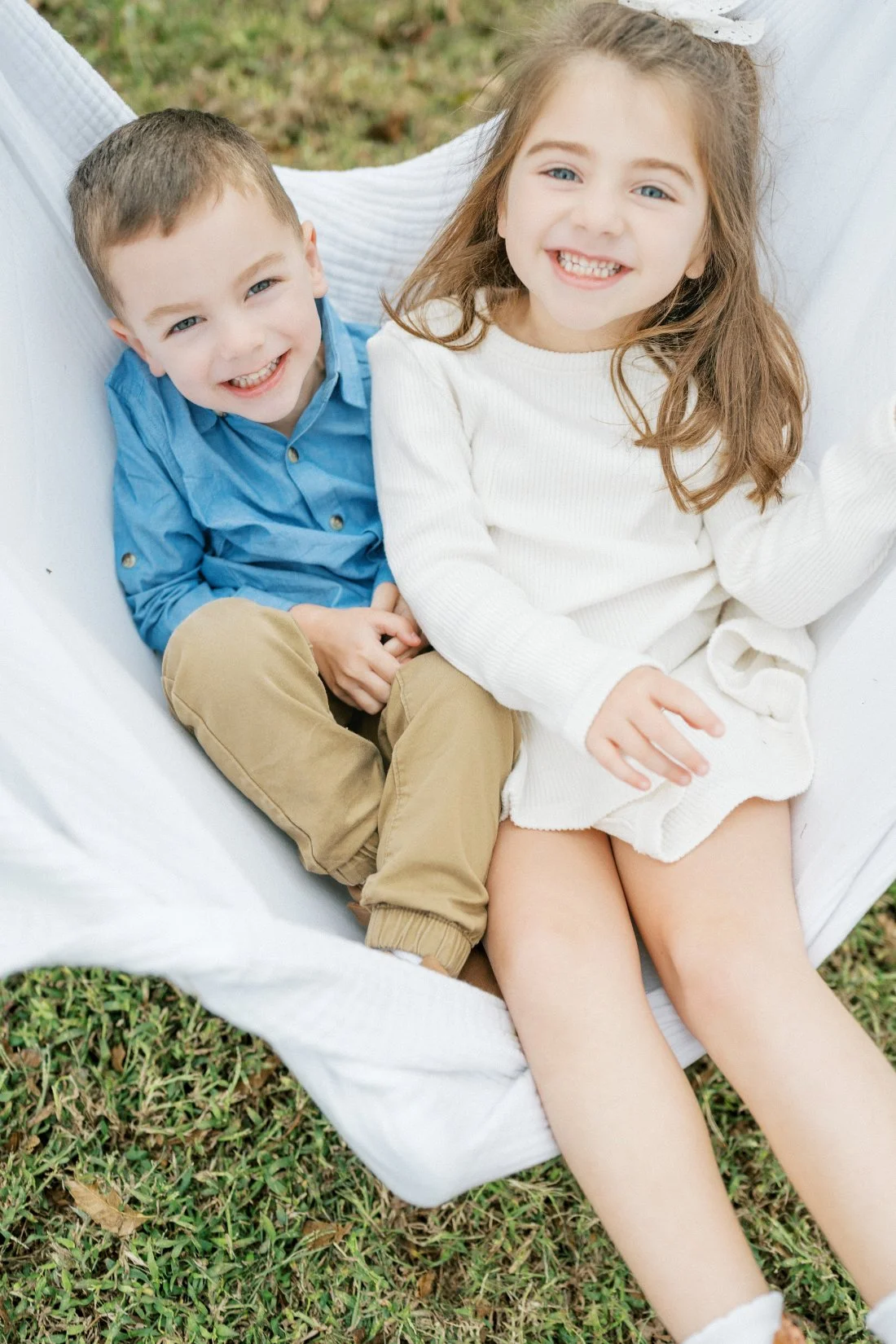 Happy siblings sitting together outdoors during a lifestyle family photography session.