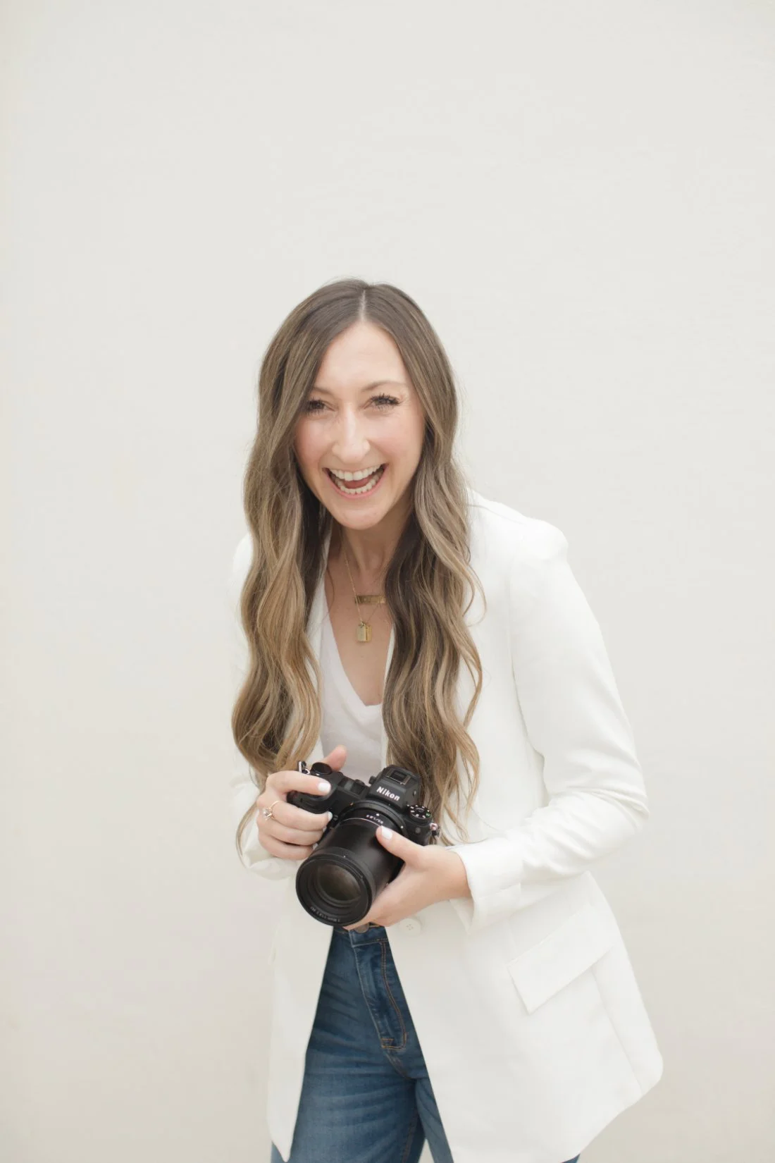 Personal brand photo of female photographer smiling and holding a Nikon camera, representing how to get photography clients through connection and personality