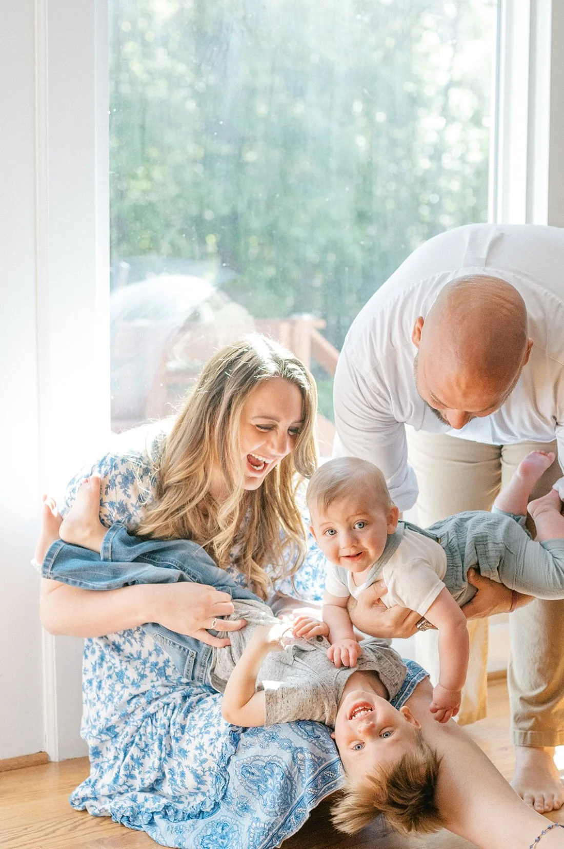 Joyful moment during a lifestyle family portraits session with parents playing with their children in natural window light.