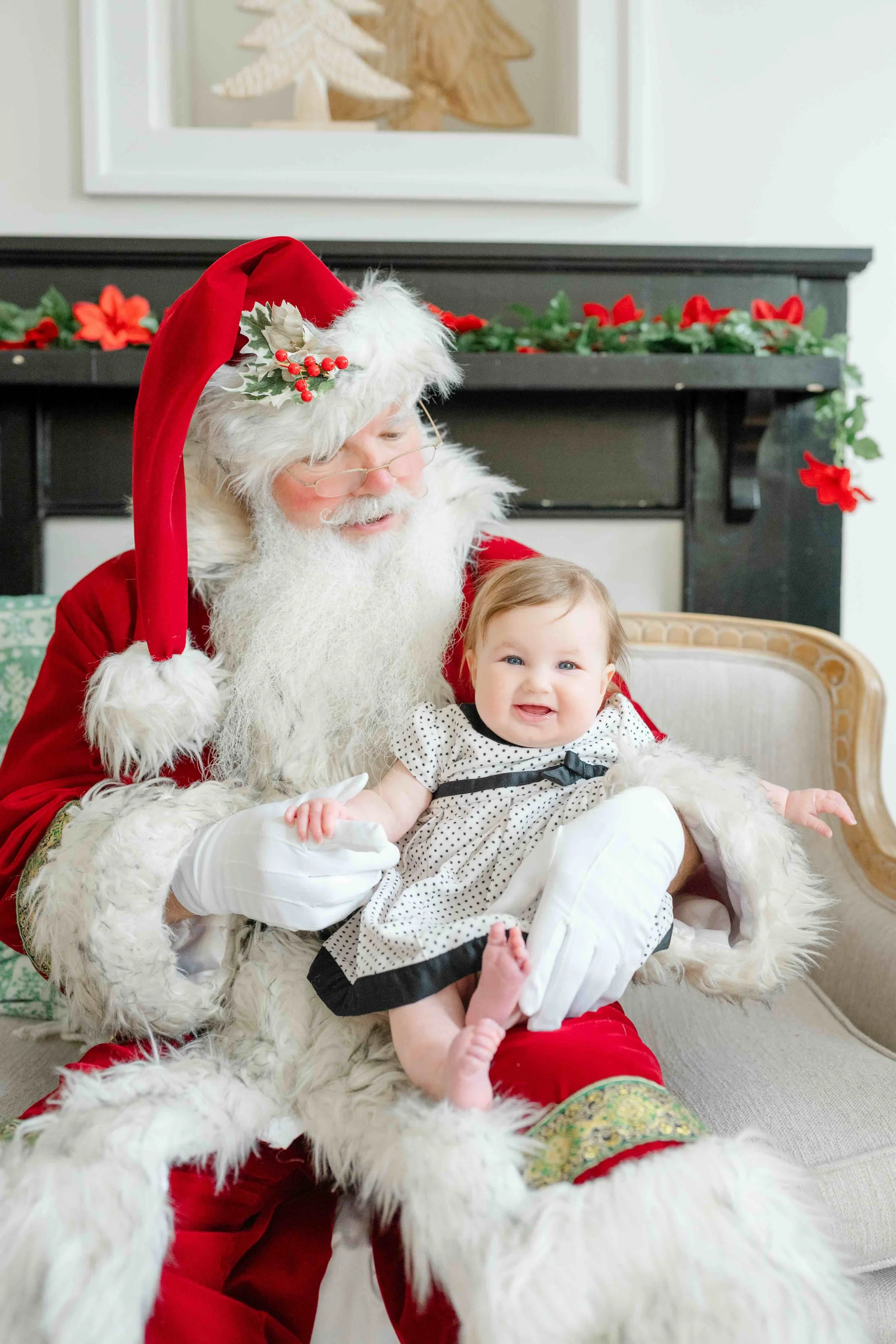 Little girl sitting on Santa's lap and holding his hand while smiling during their family Christmas Activity in Raleigh by Kelly Bullock Photography.