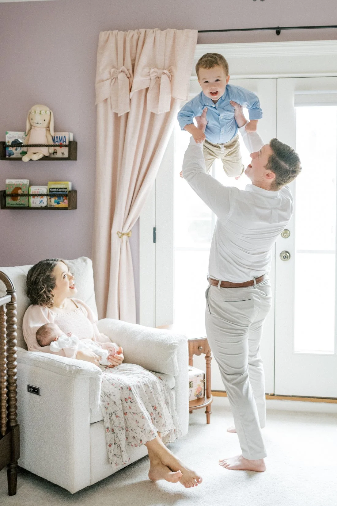 Father lifting toddler while mother holds newborn in nursery during joyful milestone checklist family photo session