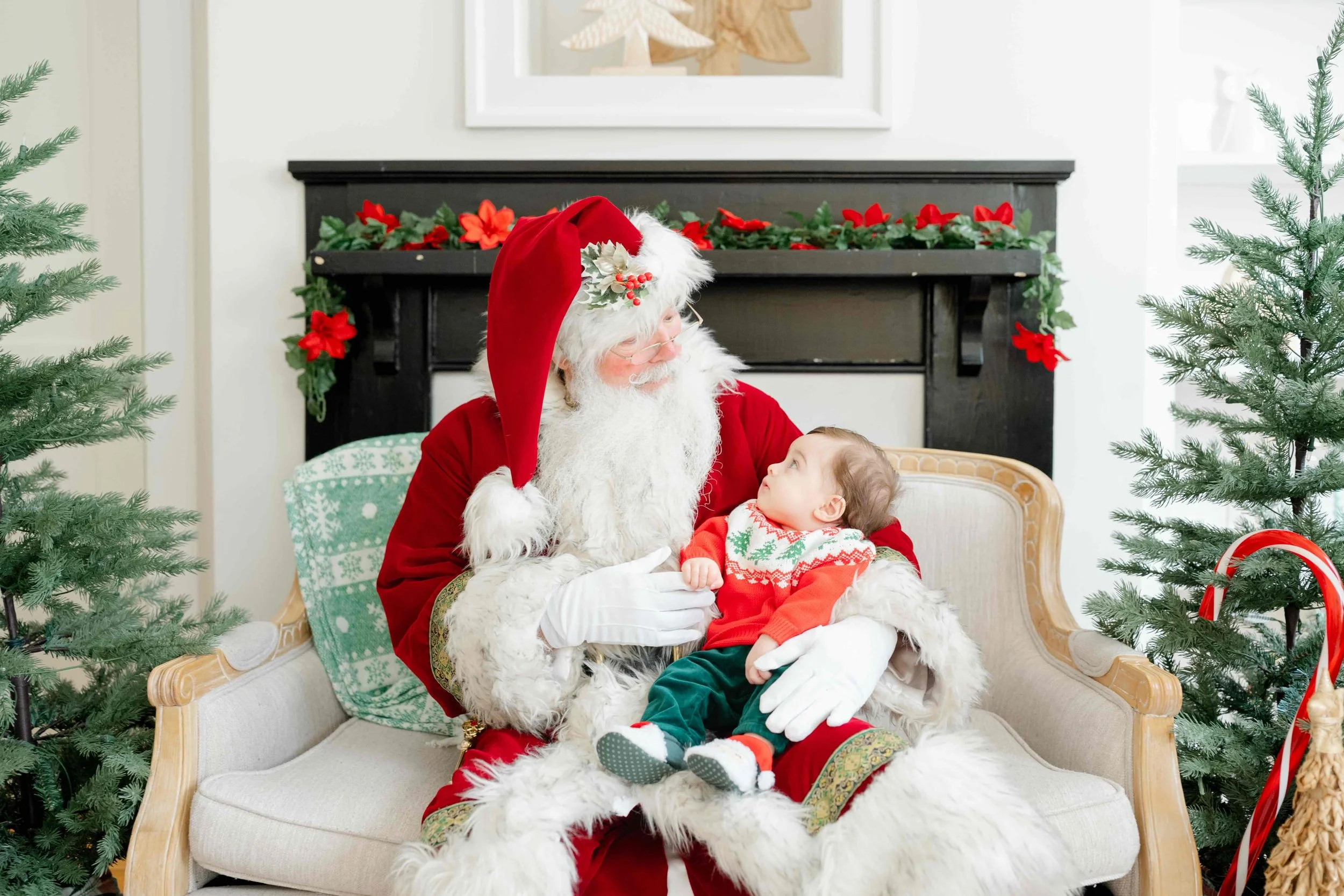 Little boy sitting in Santa's lap and they're looking at eachother, wondering when she will stop believing in Santa by Kelly Bullock Photography in Raleigh.
