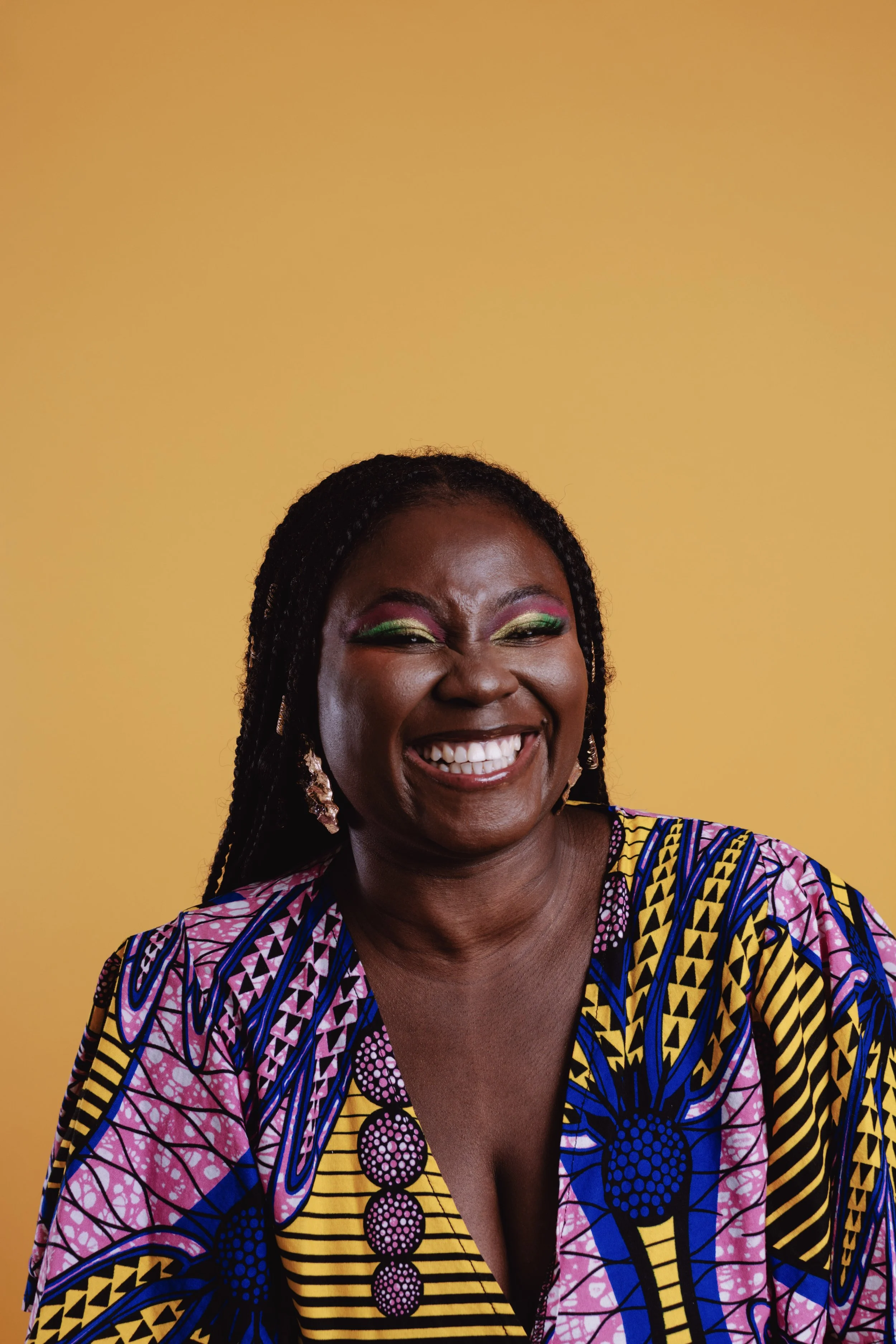 Smiling person in colorful patterned clothing against a yellow background.