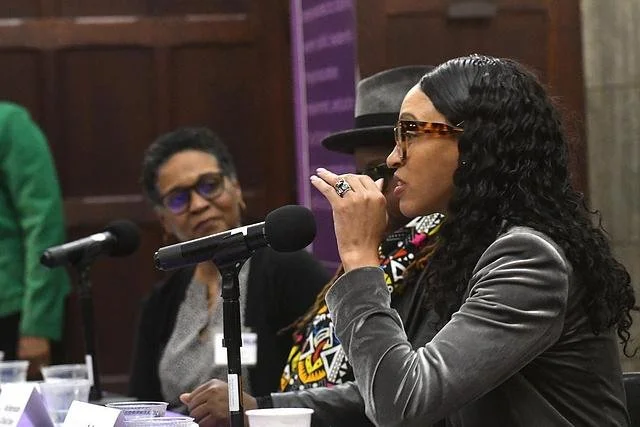 Photo of a young Black woman wearing glasses speaking into a microphone