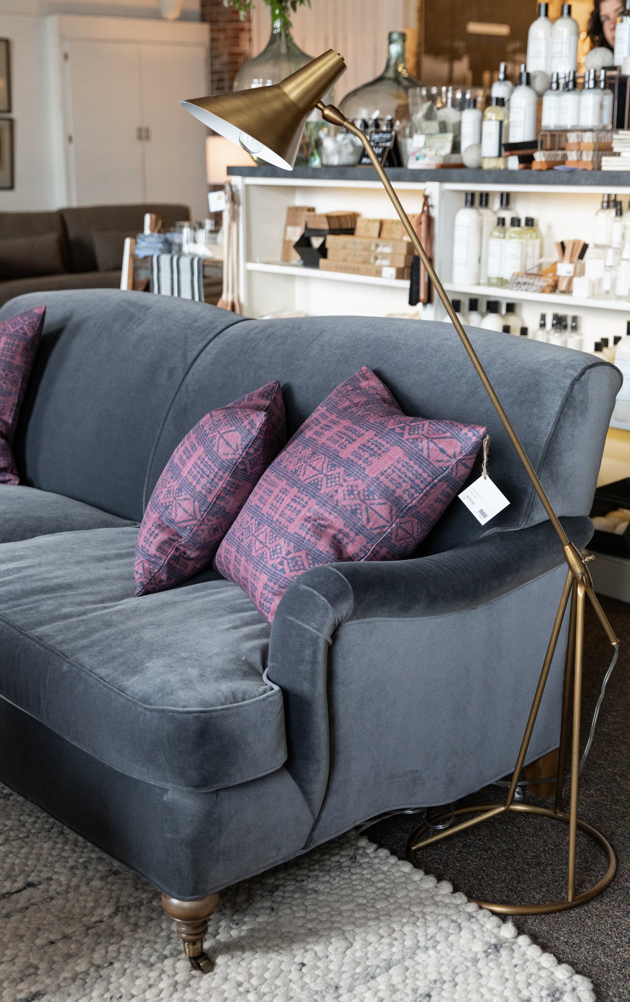 Blue velvet sofa with brass floor lamp and purple throw pillows.