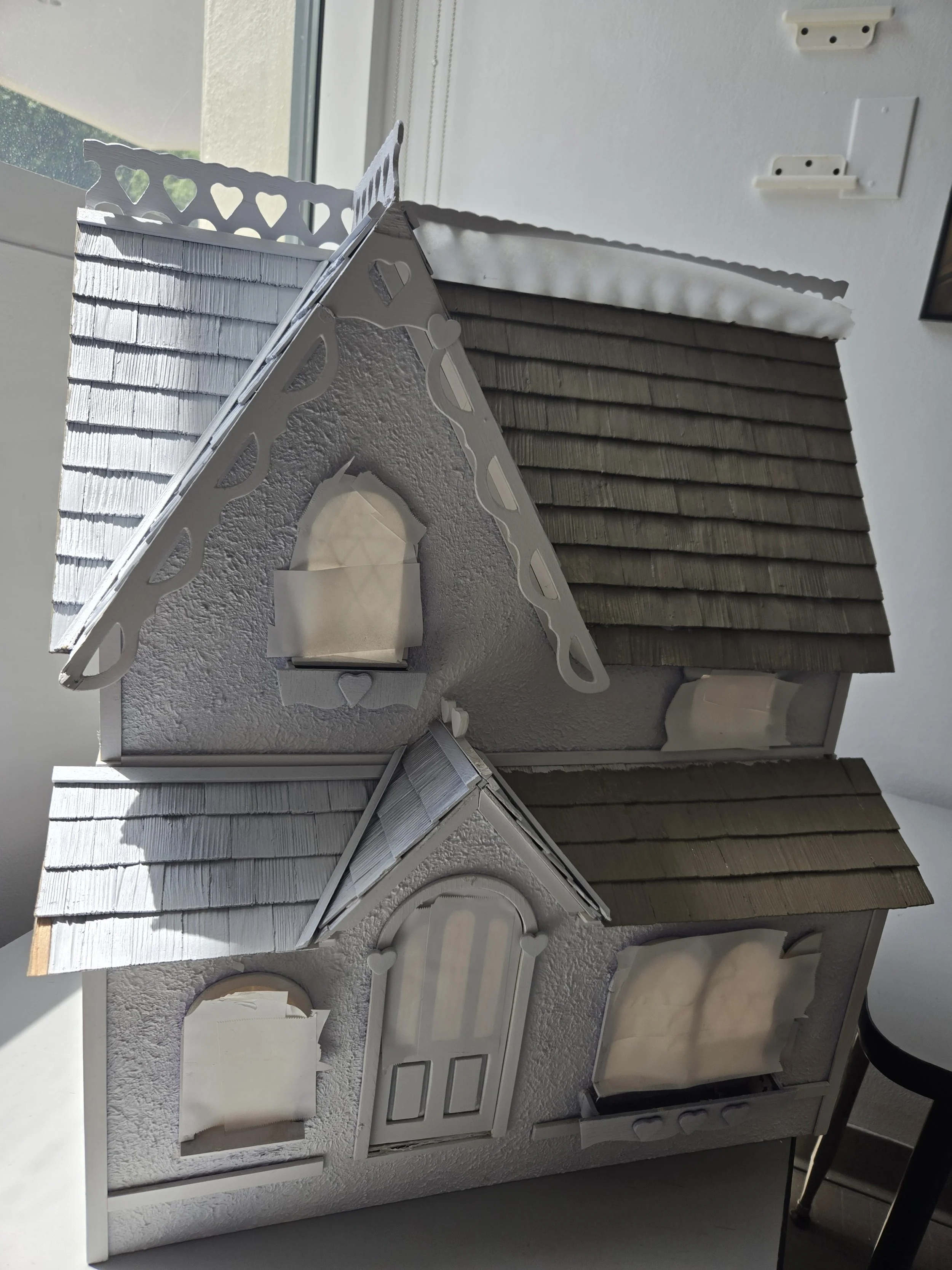 Various sample shingle siding pieces in different colors and textures laid out on a flat surface inside a room, with some paper and a white display stand