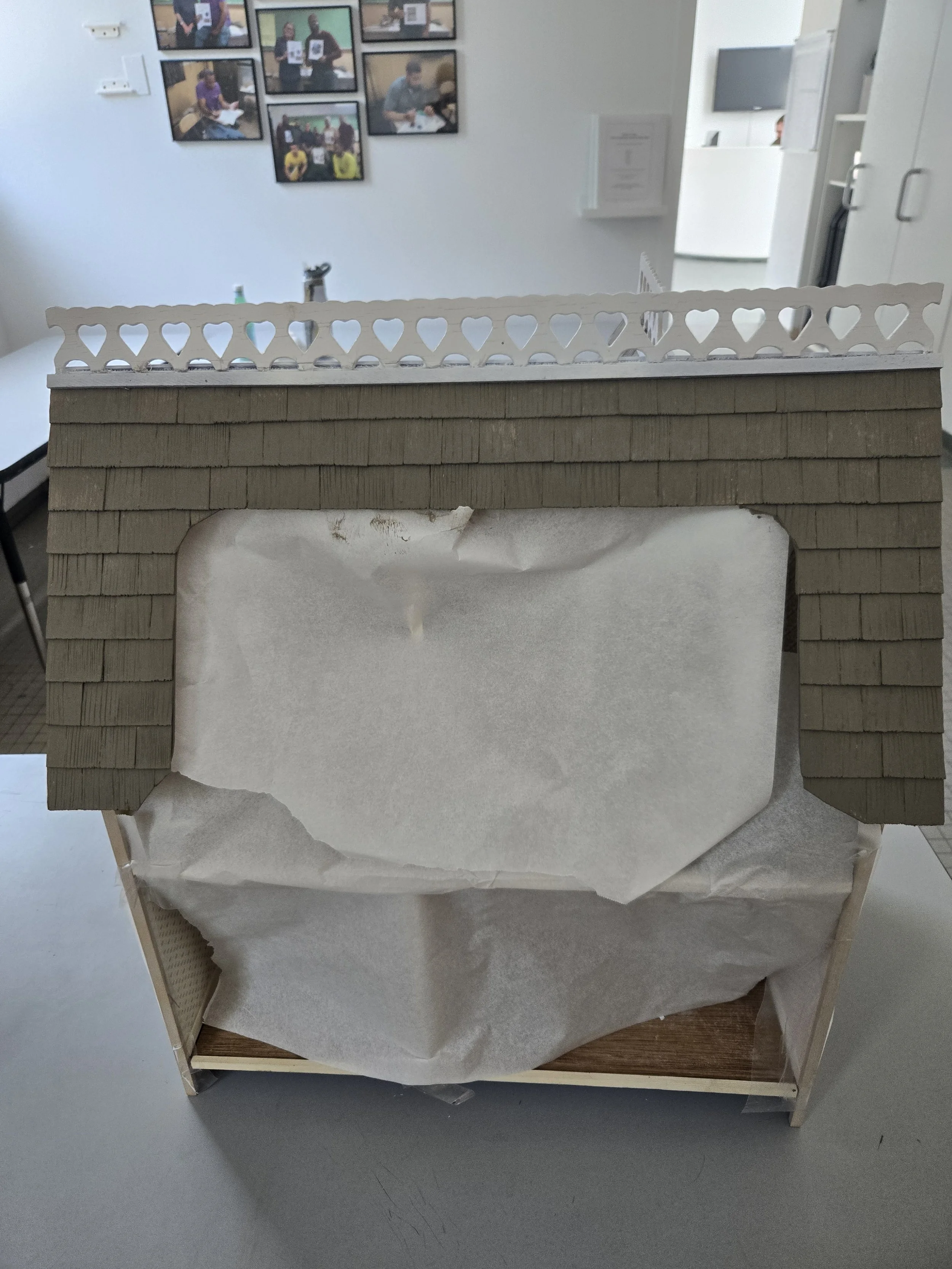 Model house with architectural design, featuring a front wall with beige bricks, a white decorative fence on top, and a partially transparent plastic covering on the bottom.