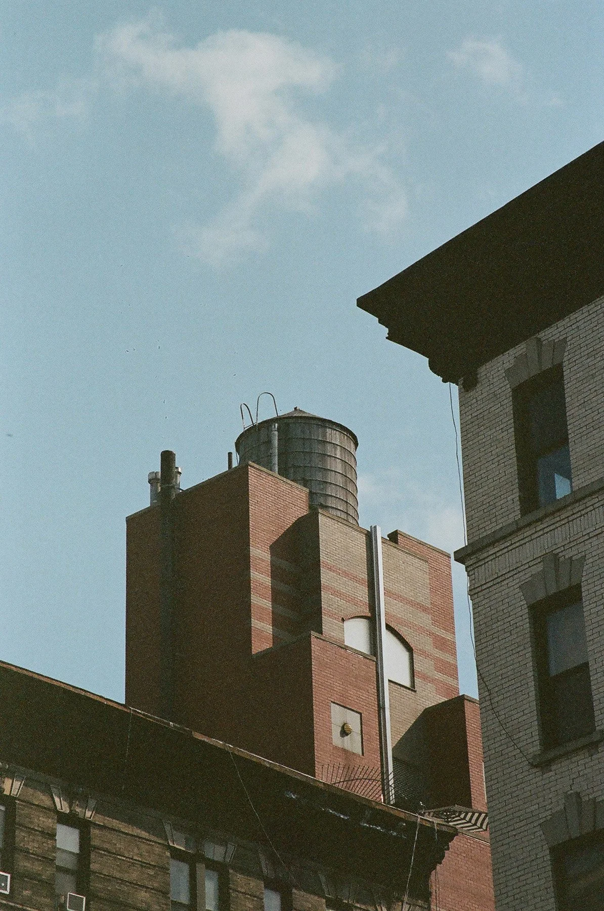 Cityscape with brick buildings and a rooftop water tower against a blue sky with some clouds.