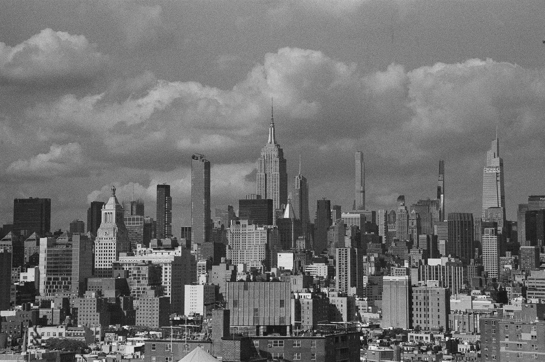 Black and white photo of a city skyline featuring the Empire State Building and various skyscrapers under a cloudy sky.