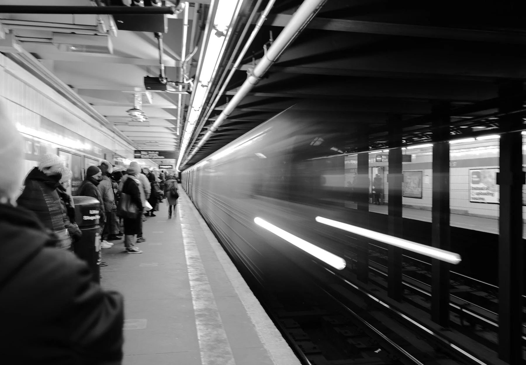 People waiting on a subway platform with a train in motion.