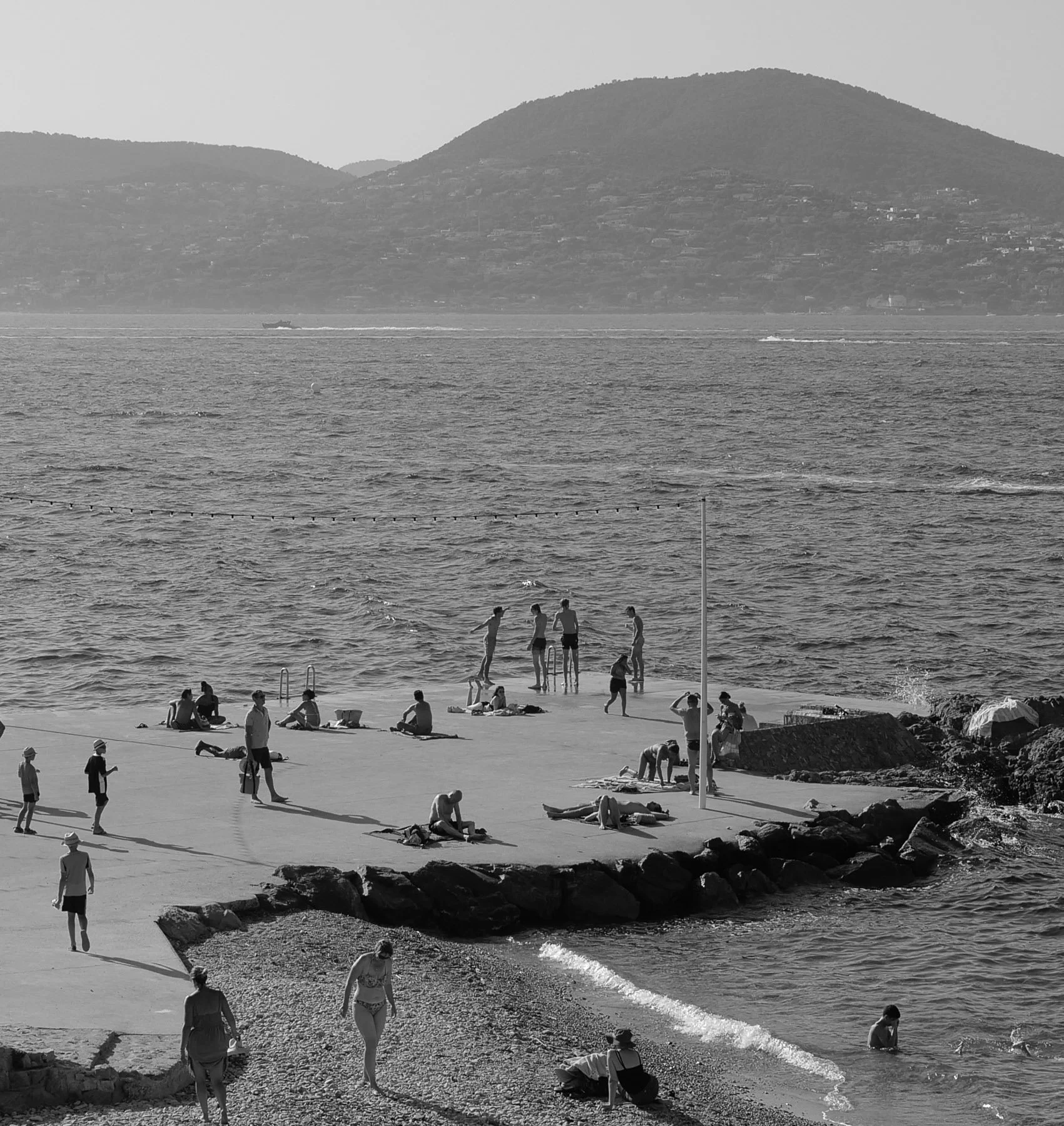 People relaxing and playing on a beach with mountains in the background.
