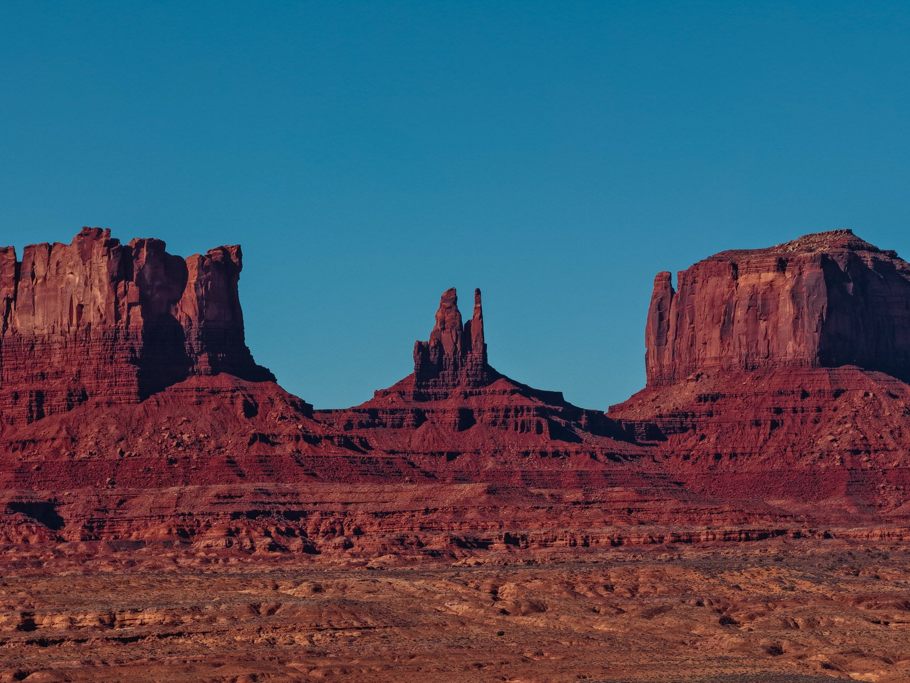 Red rock formations and mesas in Monument Valley under a clear blue sky.