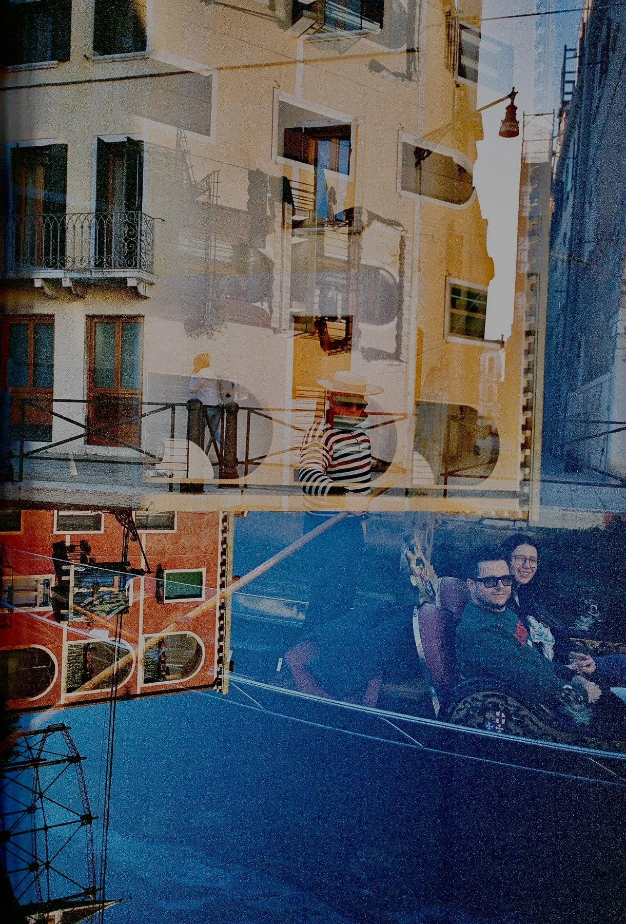 Reflection of a colorful urban scene with buildings, balconies, and people. Visible are a man and woman sitting with glasses, a person in striped shirt and straw hat walking, and various architectural elements like windows, railings, and street lamps