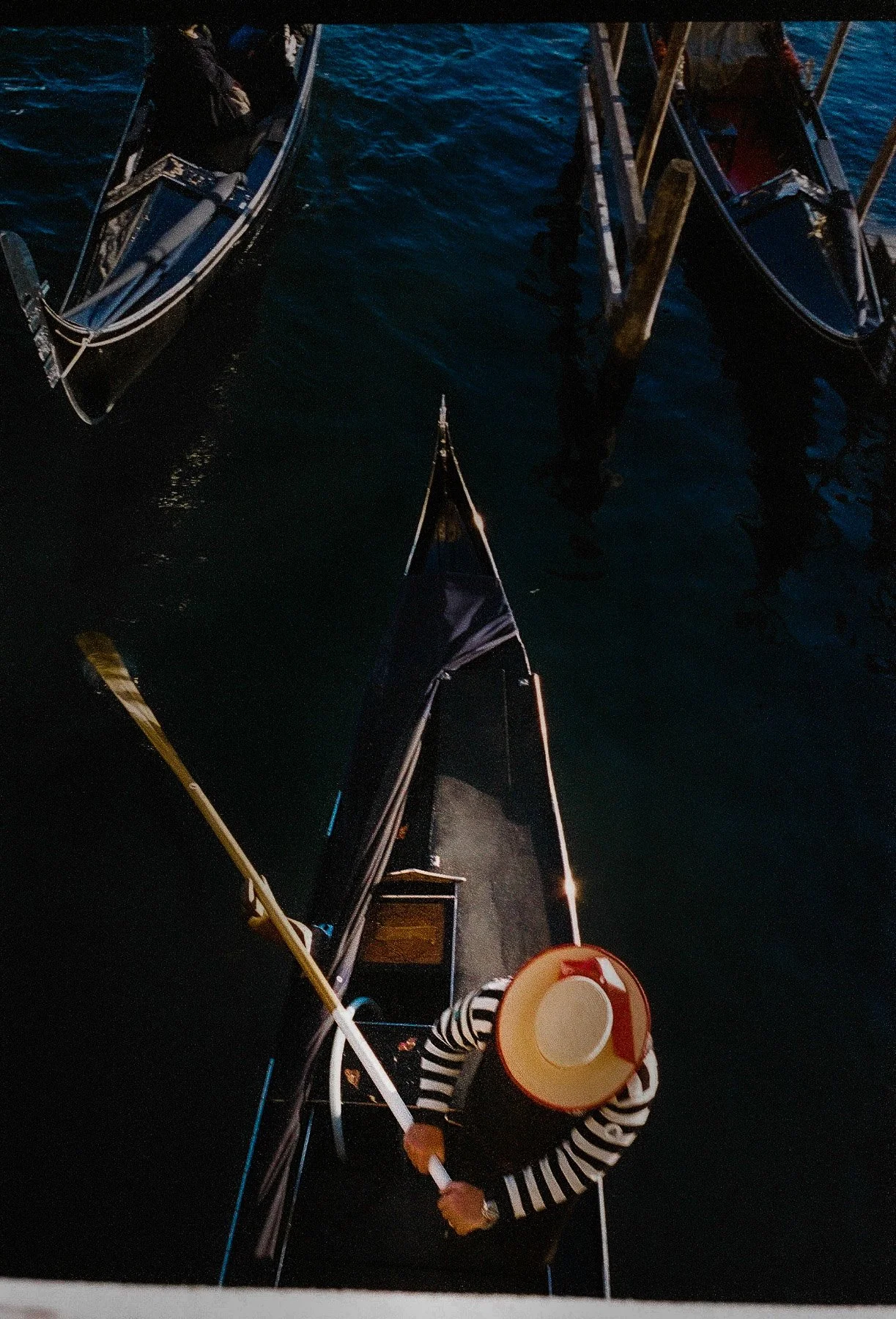 A person on a boat holding a megaphone and a paddle, wearing a striped shirt and a wide-brimmed hat, with the boat and water visible around them.