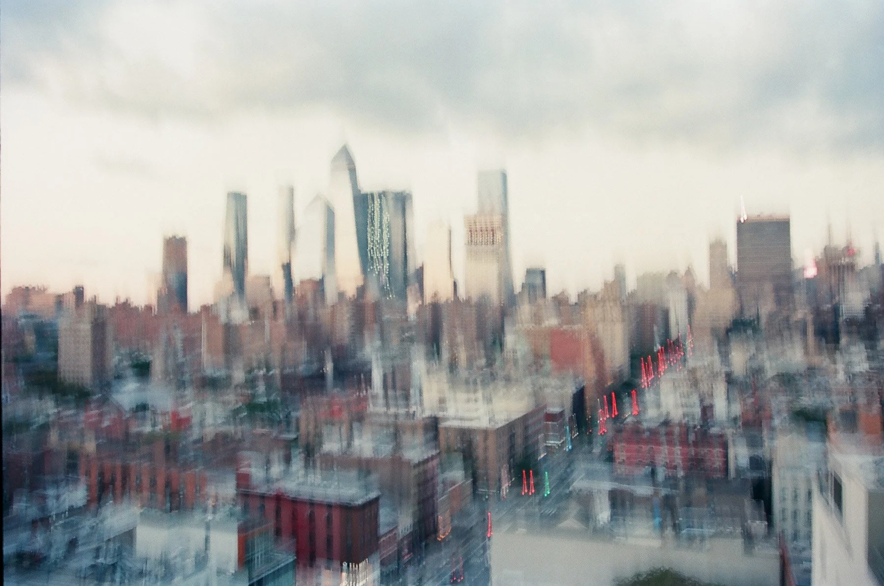 Blurry cityscape with tall skyscrapers on a cloudy day, with lights on in some buildings.