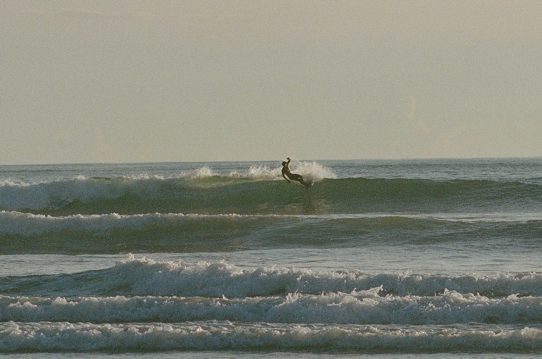 A person surfing on a wave in the ocean during sunset or sunrise.