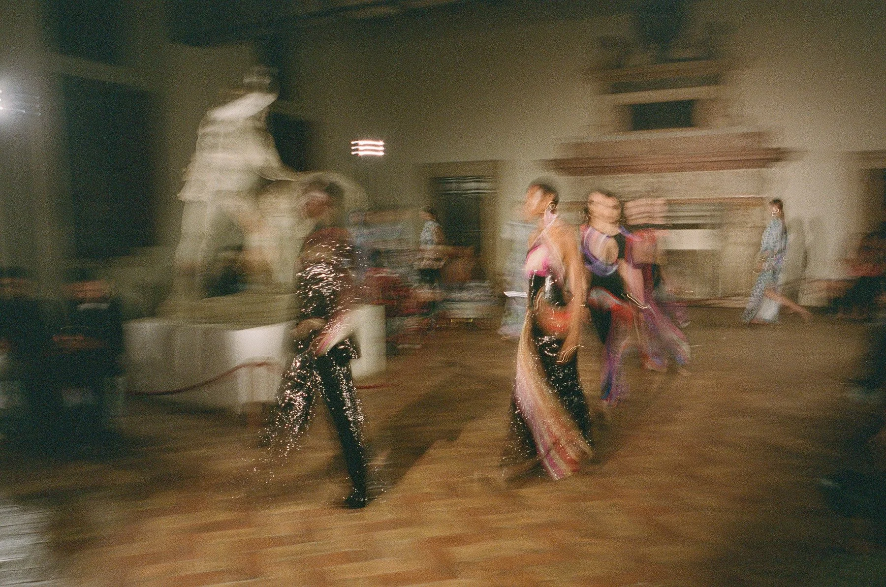 People dancing in an indoor venue with blurred motion, wearing colorful and shiny outfits, with vivid lighting and a warm ambiance.