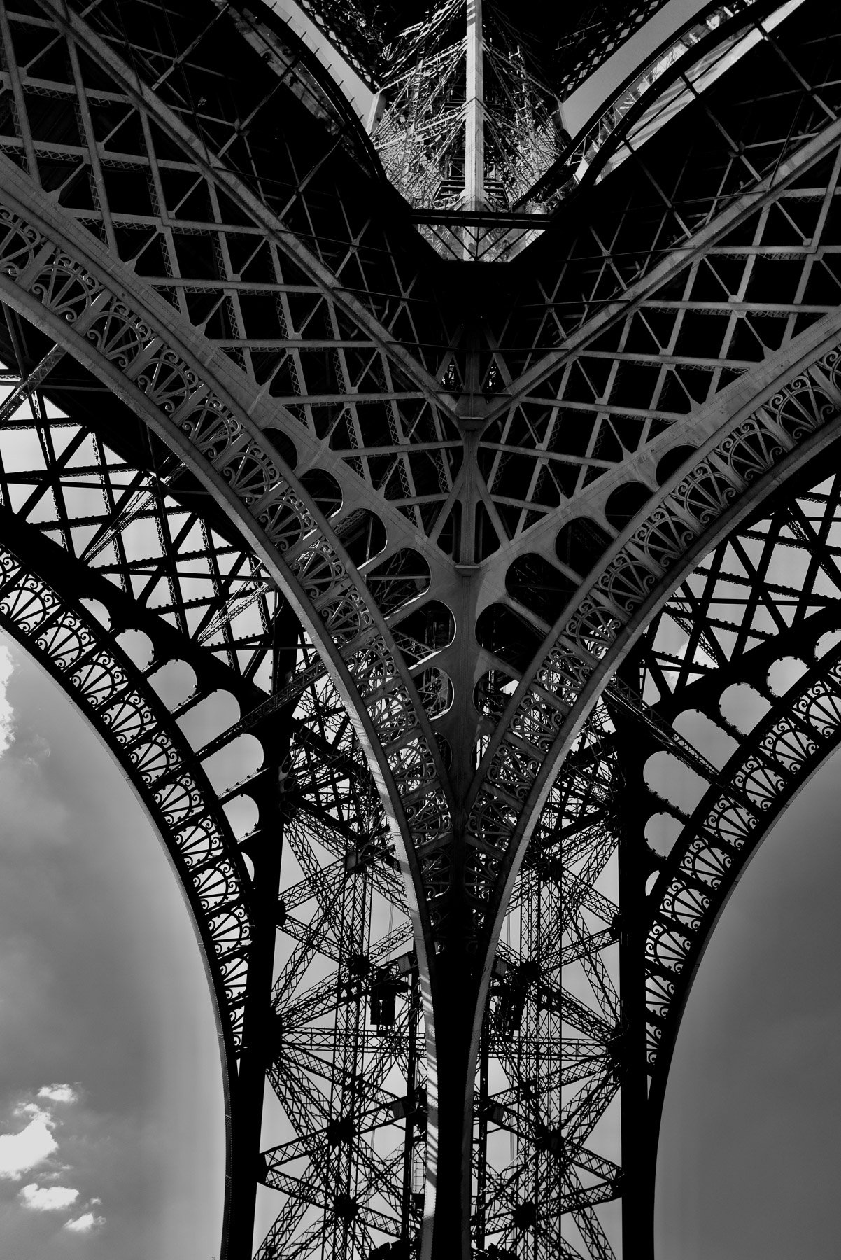 Black and white photograph of the underside of the Eiffel Tower showing intricate metal framework and lattice structure.