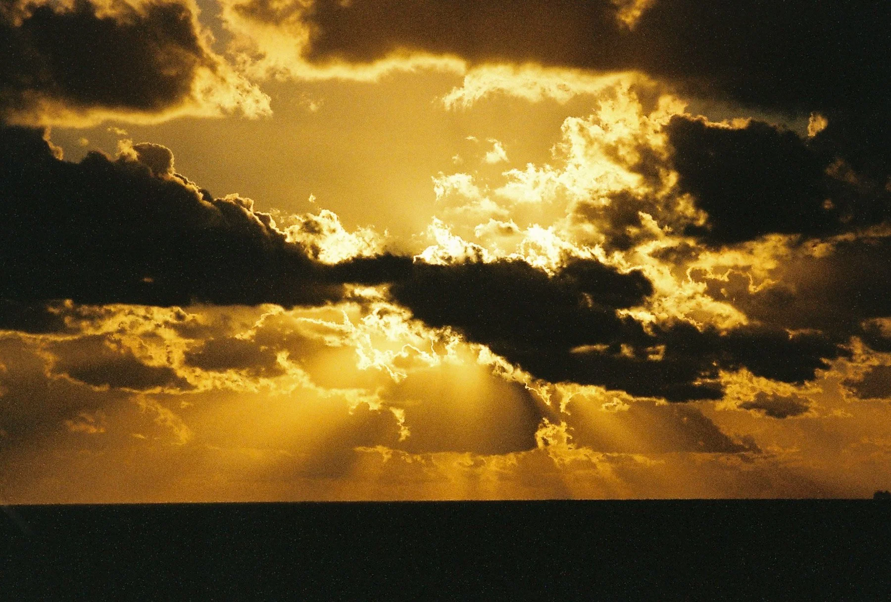 A view of the sky at sunset with dark clouds and golden sunlight breaking through.