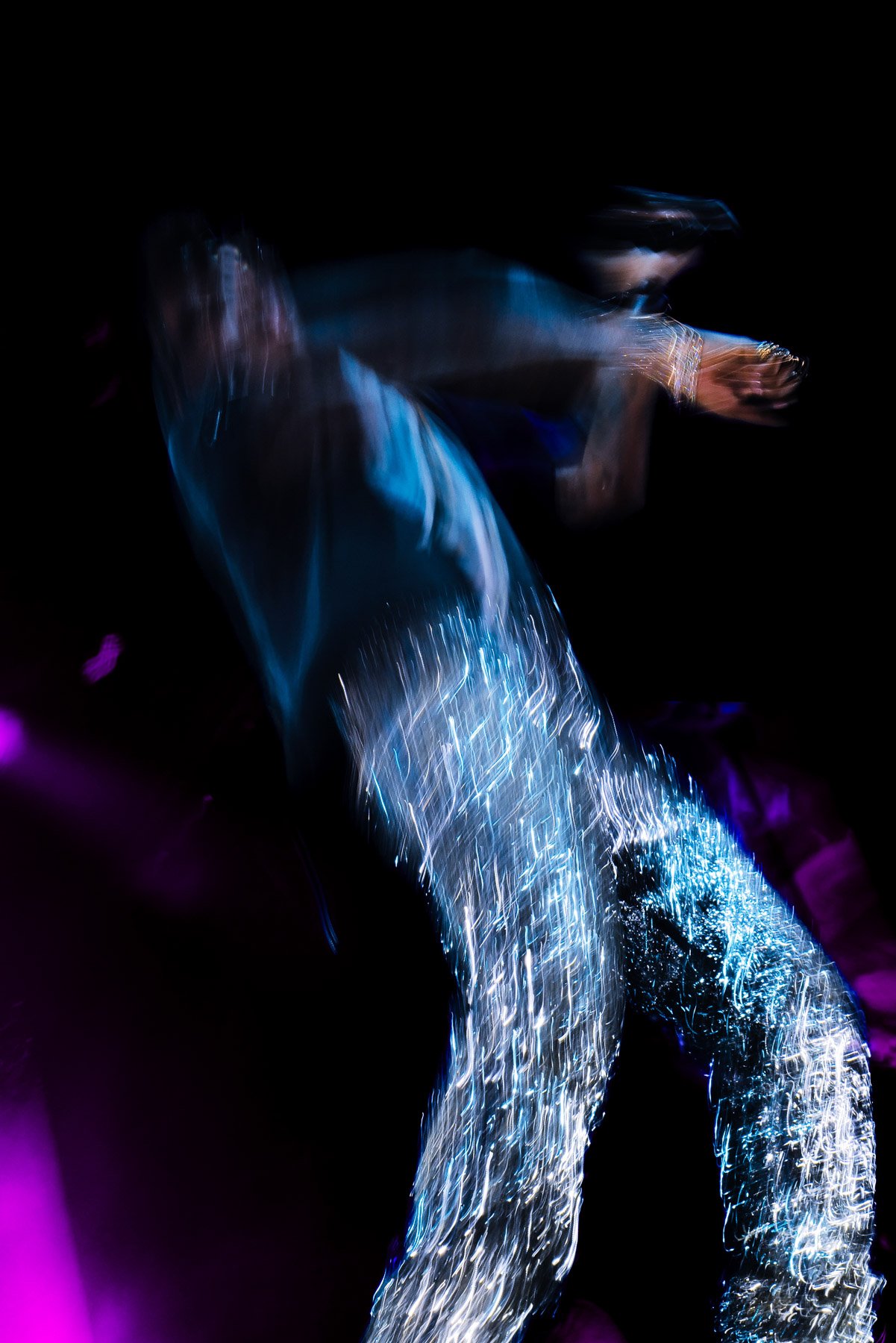 Blurred image of a person with water or light reflecting on their body in a dark environment, creating a dynamic, abstract visual effect.