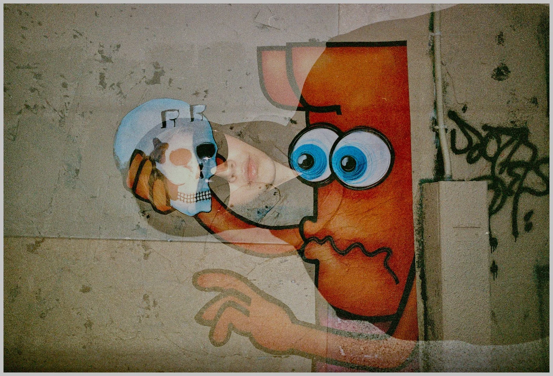 Street art graffiti of a cartoon character with large blue eyes and a red face, overlaid with a faded image of a woman's face in profile on a weathered wall.