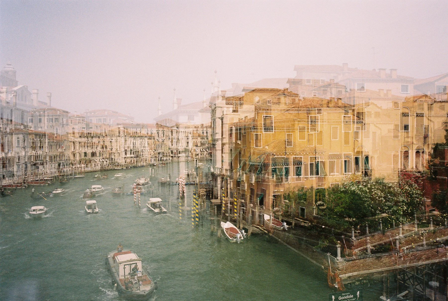 A double exposure photograph of a canal in Venice with boats and colorful buildings, overlaid with another image of more buildings and rooftops.
