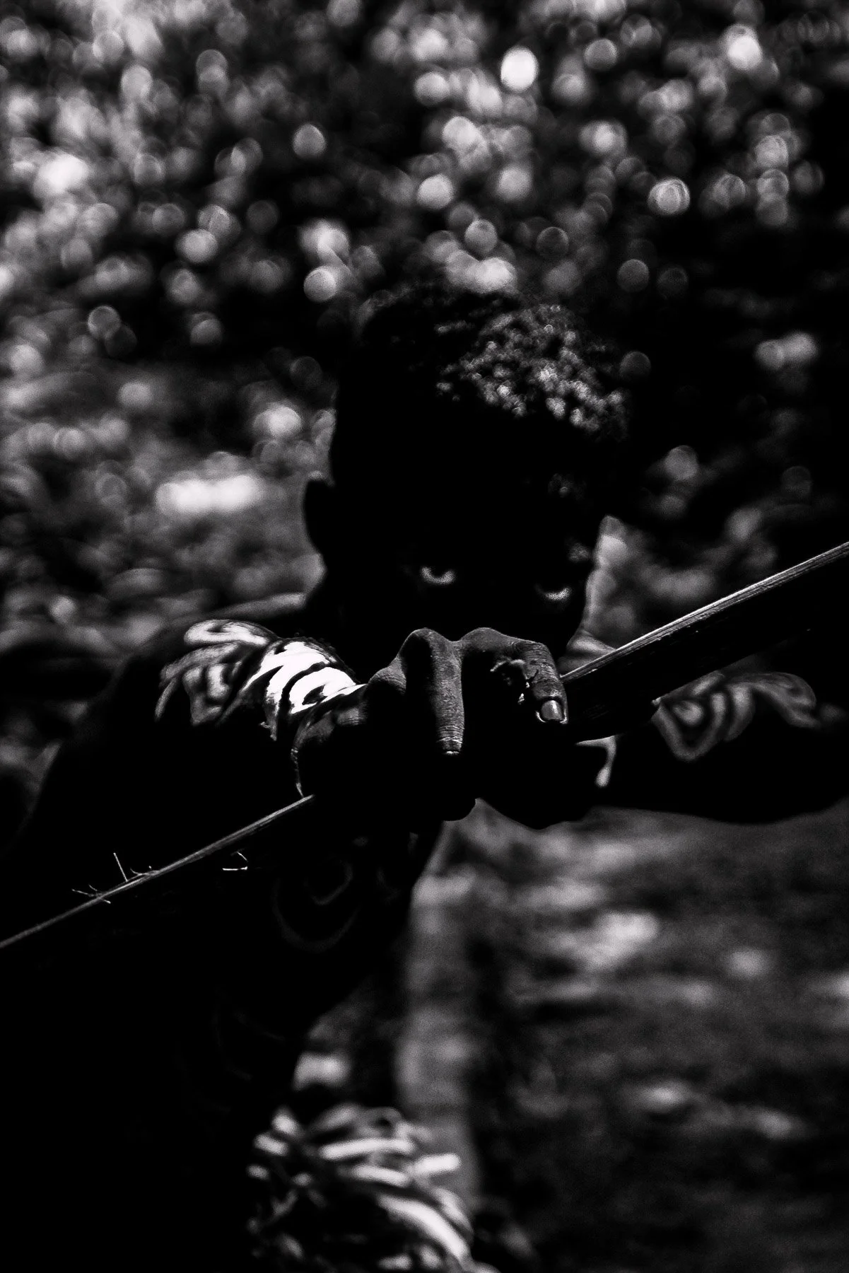 A dark, black-and-white photo of a person holding a stick or rod, with a background of out-of-focus, light-reflecting water or ground surface.