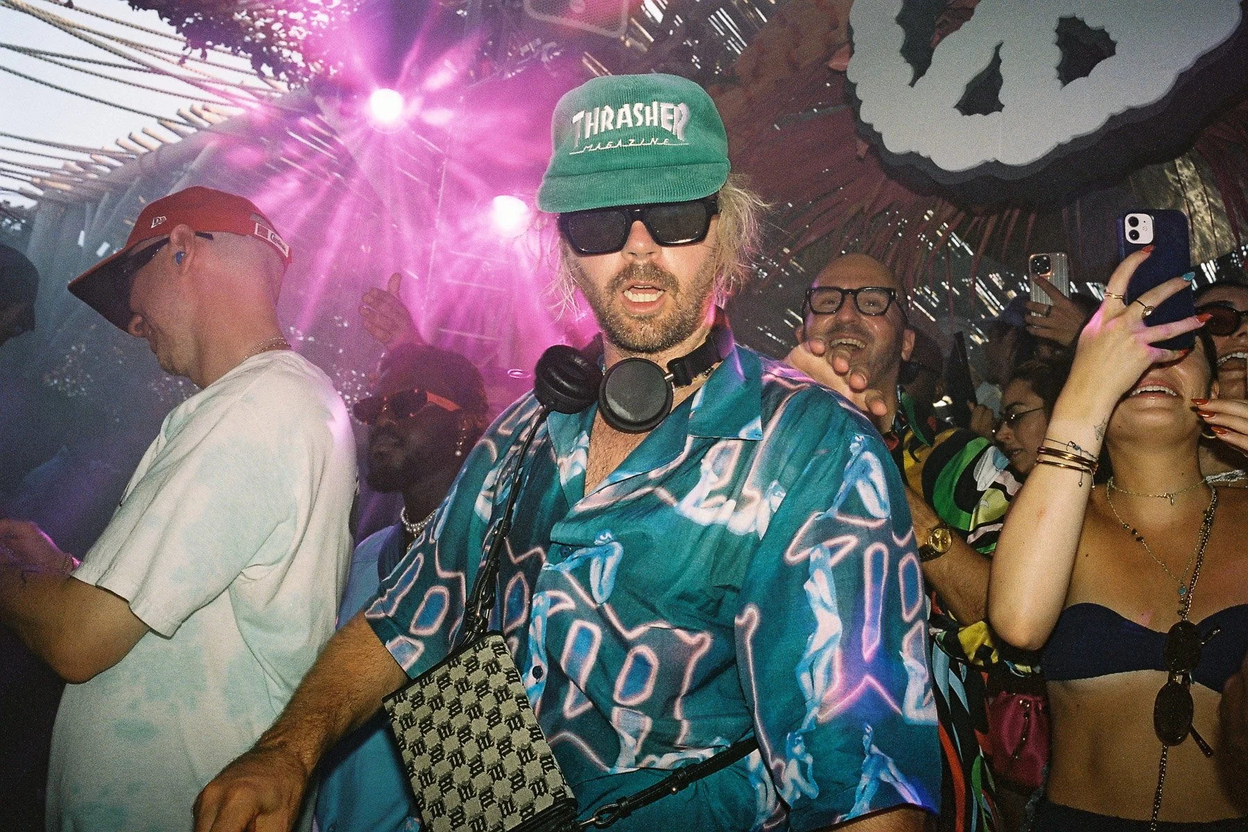A group of people at a party or club, dancing and enjoying themselves, with pink lighting and a wooden ceiling with hanging decorations in the background.