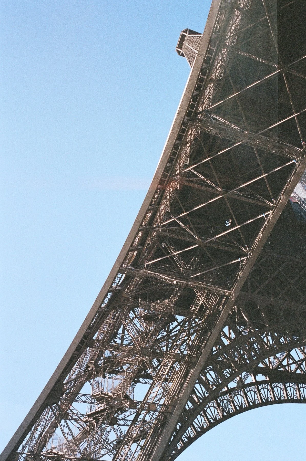 Close-up of the Eiffel Tower's iron lattice structure from below, with a clear blue sky in the background.