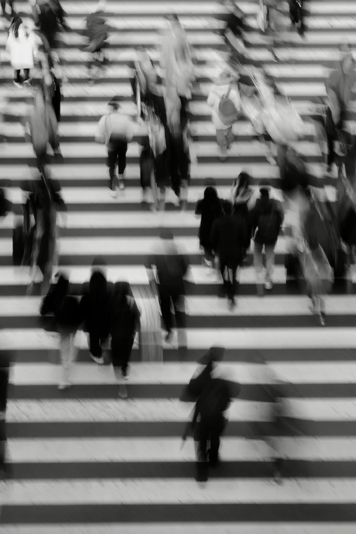 Black and white aerial view of people walking across a striped crosswalk in a busy urban area.