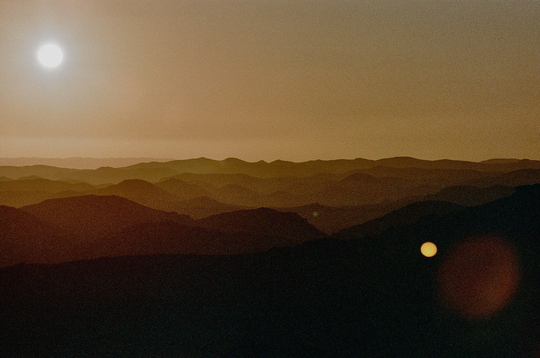 Moon shining over a landscape of mountainous hills at night with a visible lower moon in the sky.