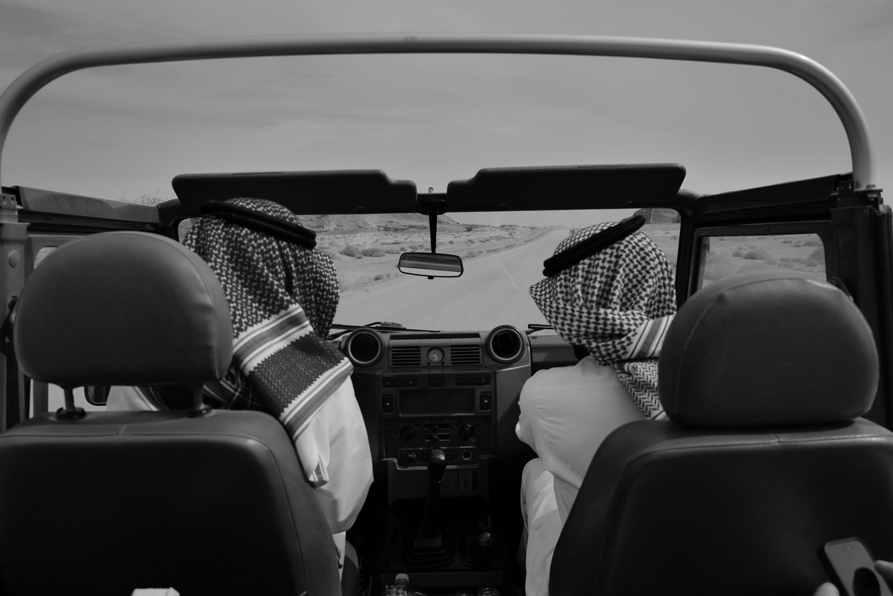 Two men wearing keffiyeh headscarves driving a jeep through a desert landscape.